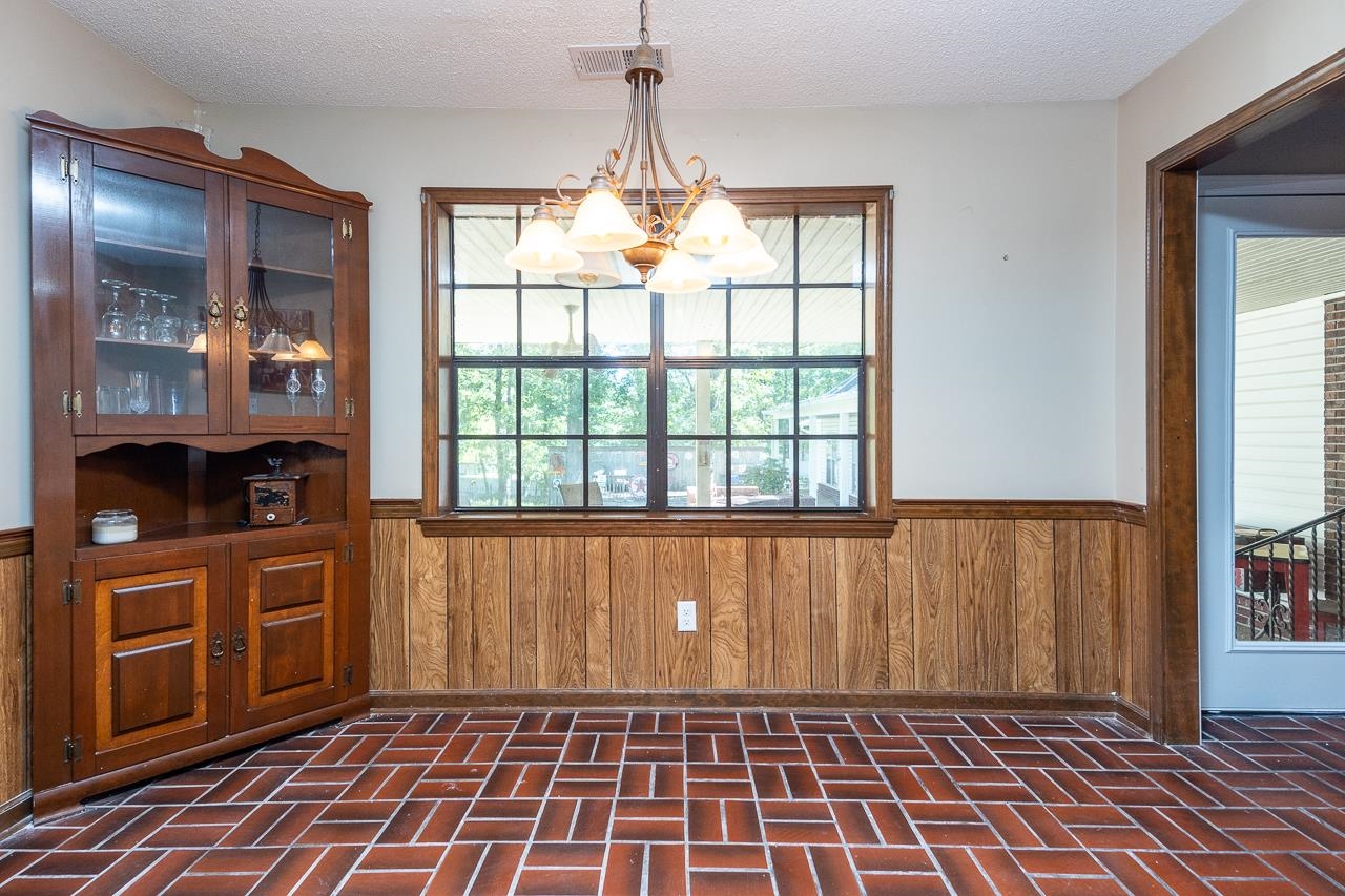 Unfurnished dining area with an inviting chandelier, wooden walls, plenty of natural light, and a textured ceiling