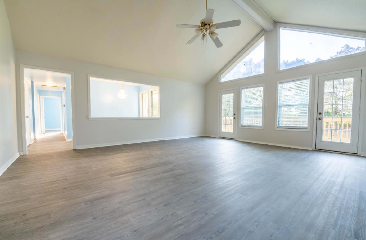 Unfurnished living room featuring ceiling fan, hardwood / wood-style floors, beam ceiling, and high vaulted ceiling