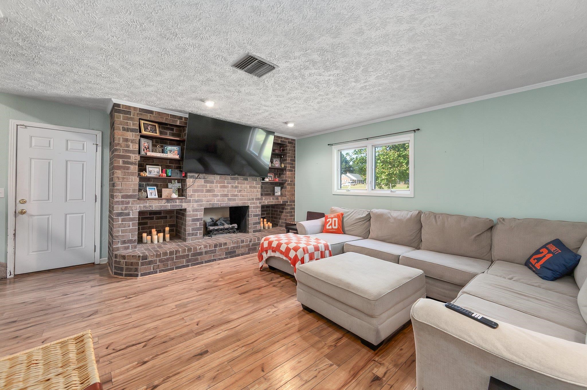 Living room featuring a textured ceiling, a fireplace, crown molding, and light hardwood / wood-style flooring