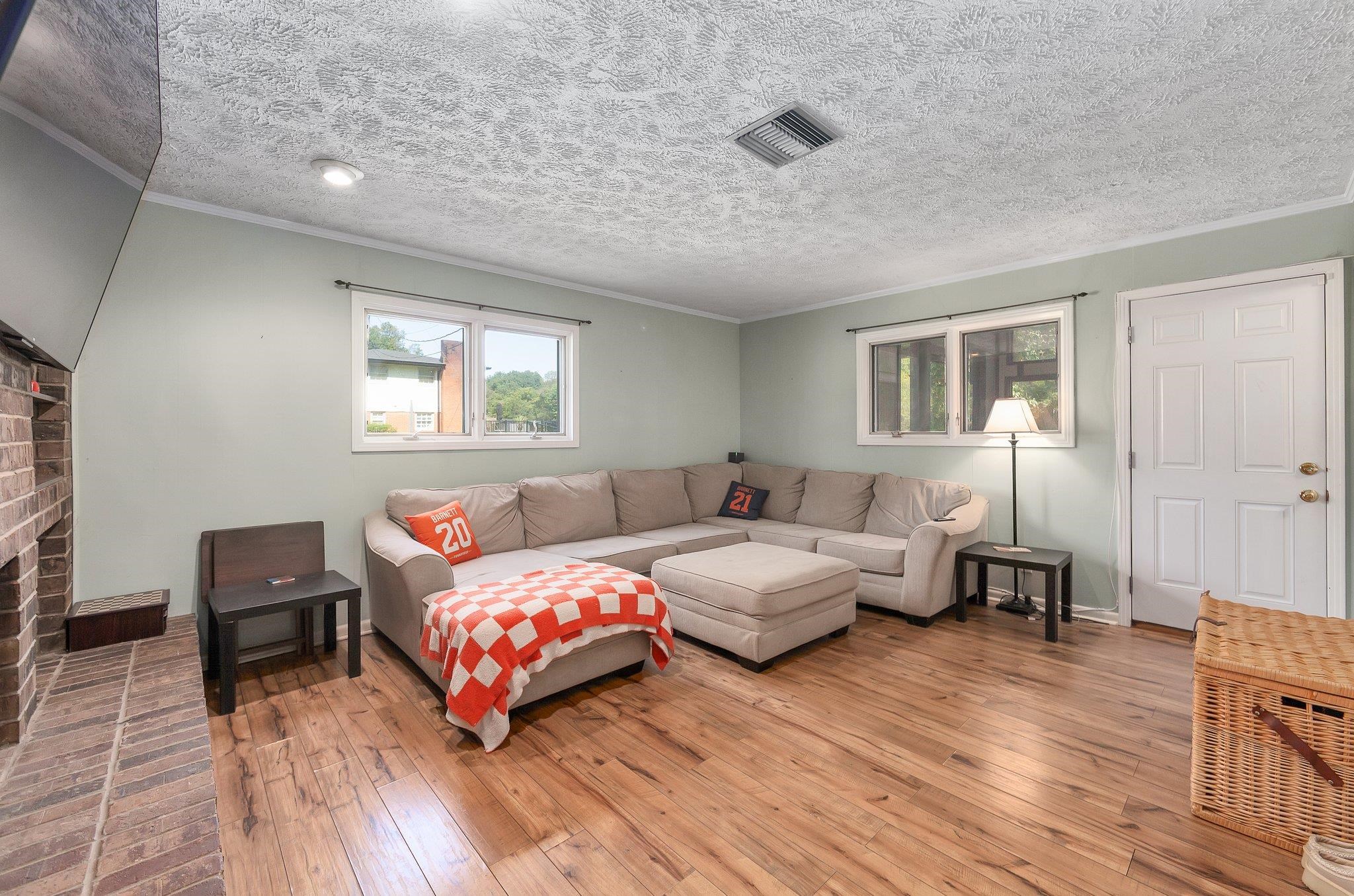 Living room featuring a brick fireplace, light hardwood / wood-style floors, crown molding, and a textured ceiling