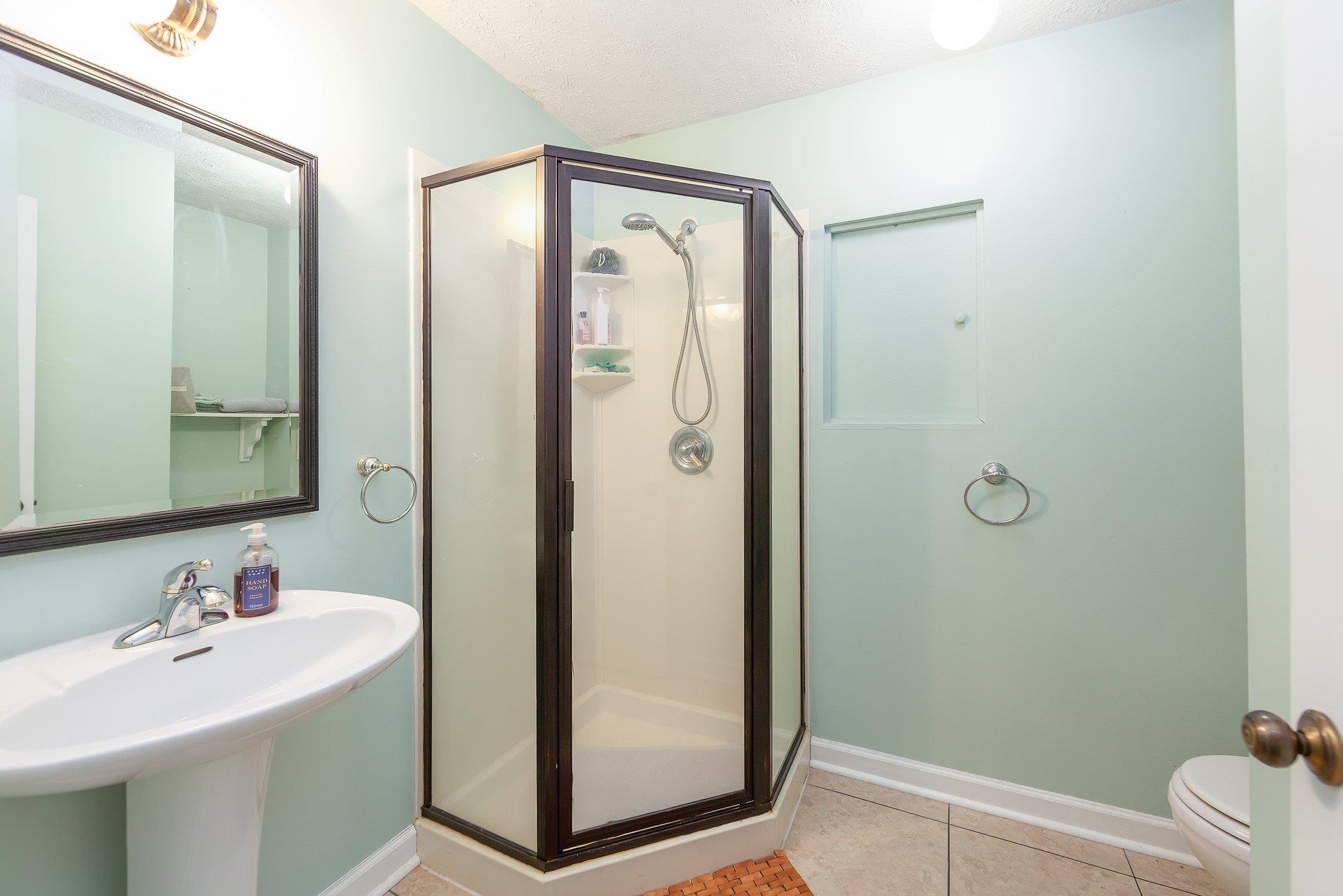 Bathroom featuring tile patterned flooring, a shower with door, toilet, and a textured ceiling
