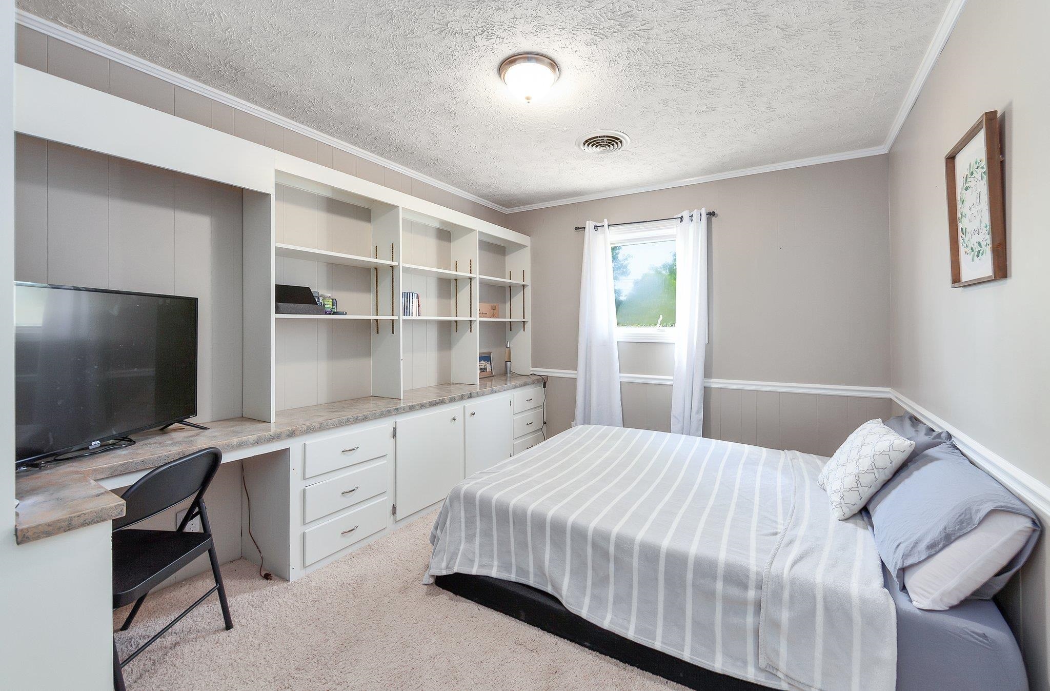 Bedroom with light colored carpet, a textured ceiling, built in desk, and ornamental molding