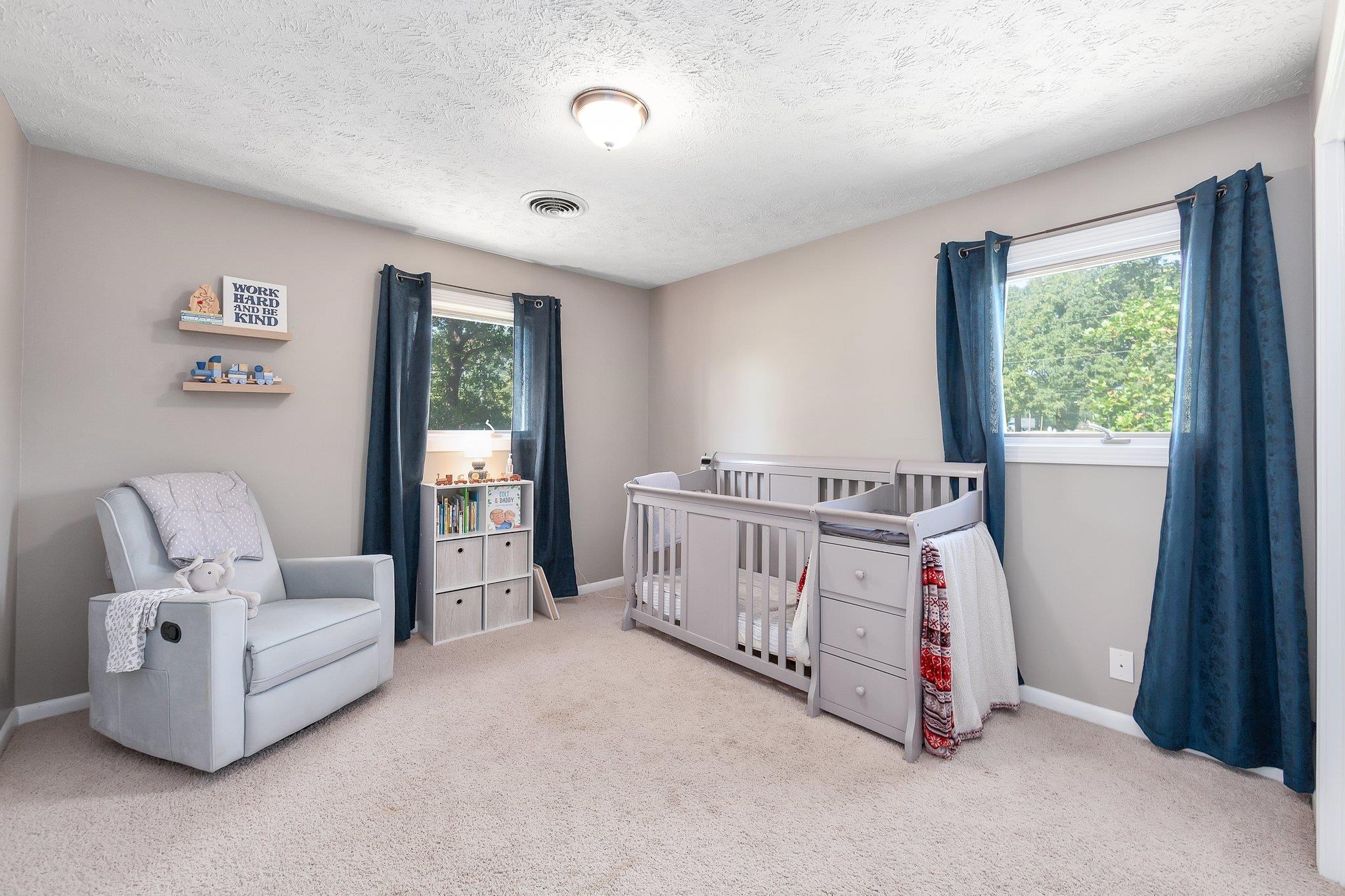 Bedroom featuring a nursery area, light colored carpet, and multiple windows
