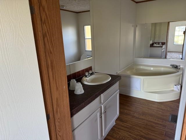 Bathroom with ornamental molding, vanity, a bath, and wood-type flooring