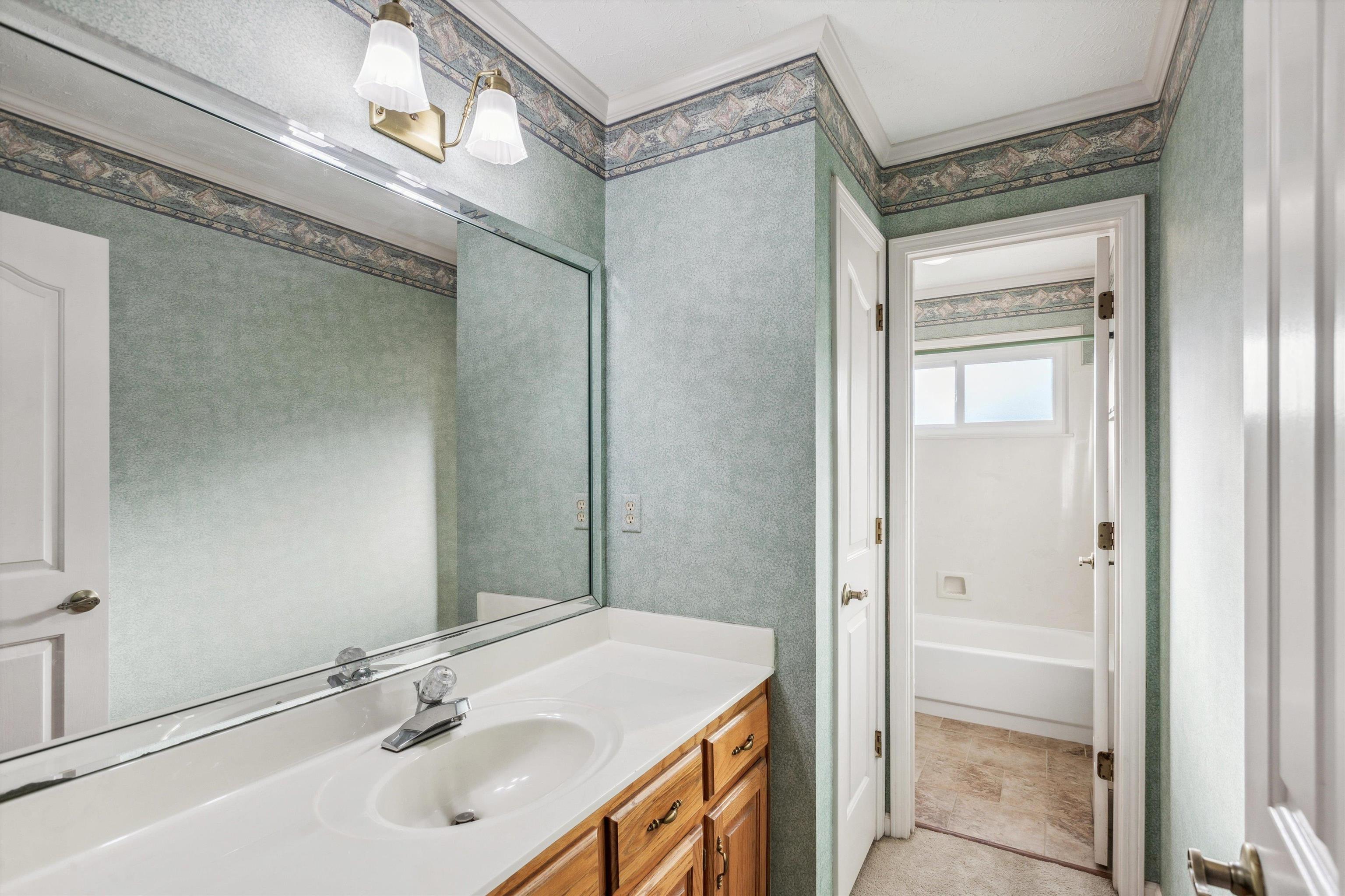 Bathroom with tile patterned flooring, crown molding, vanity, and a bathing tub