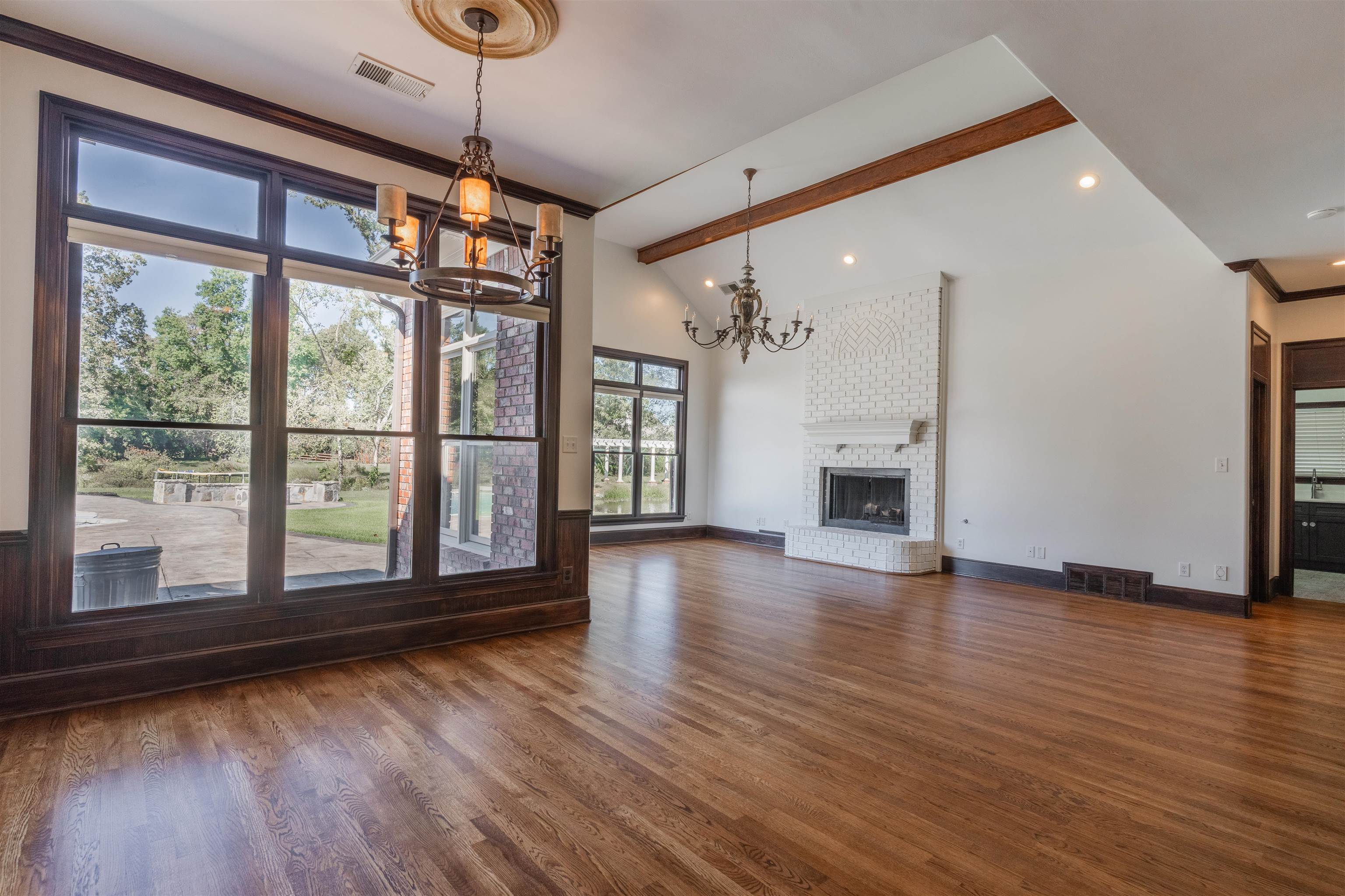 Unfurnished living room with dark hardwood / wood-style floors, lofted ceiling with beams, a notable chandelier, a fireplace, and crown molding