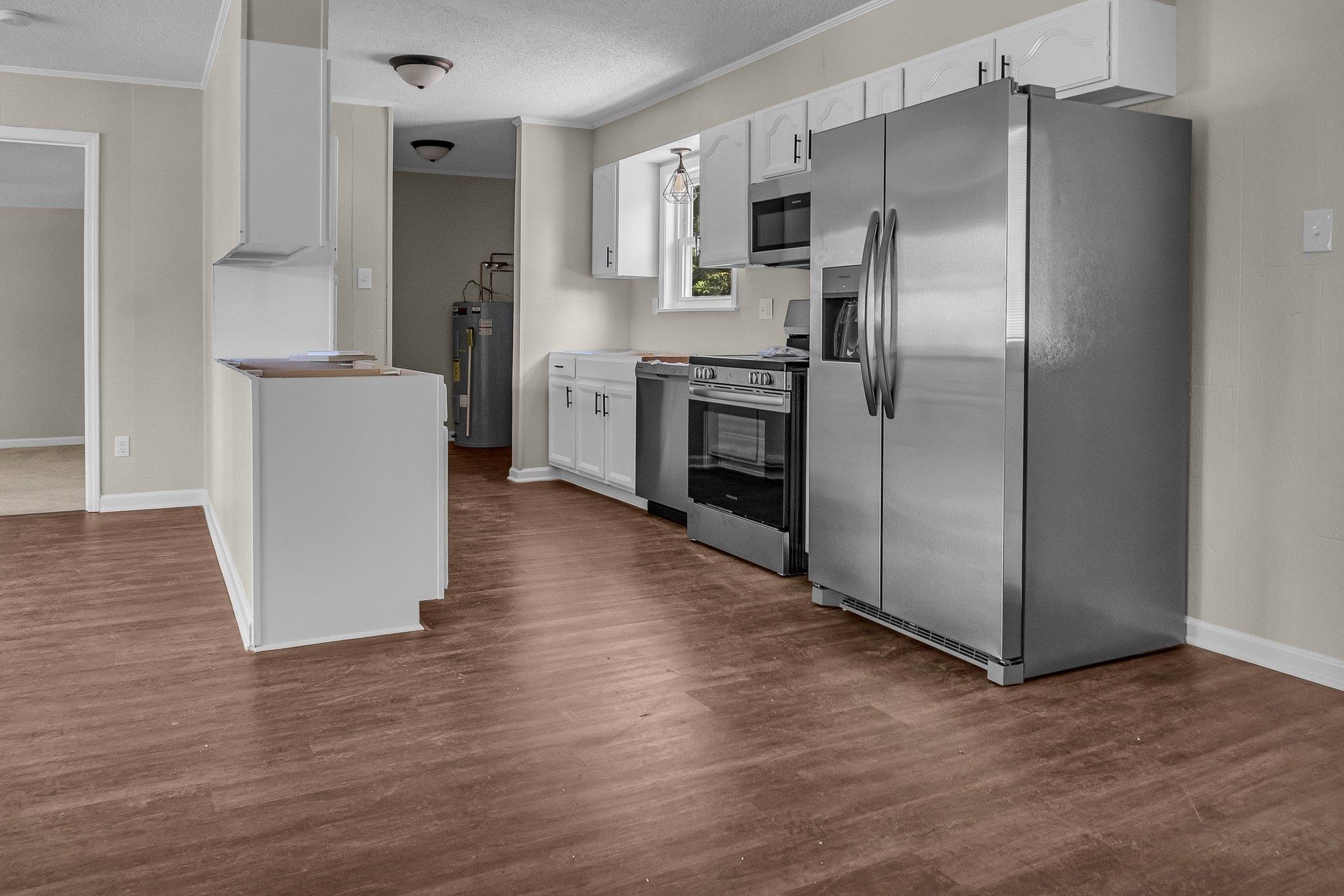 Kitchen with electric water heater, stainless steel appliances, dark hardwood / wood-style floors, and white cabinetry