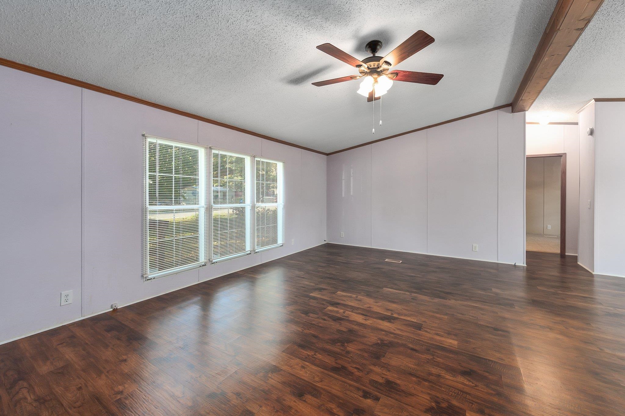 Empty room with ceiling fan, ornamental molding, a textured ceiling, and dark wood-type flooring