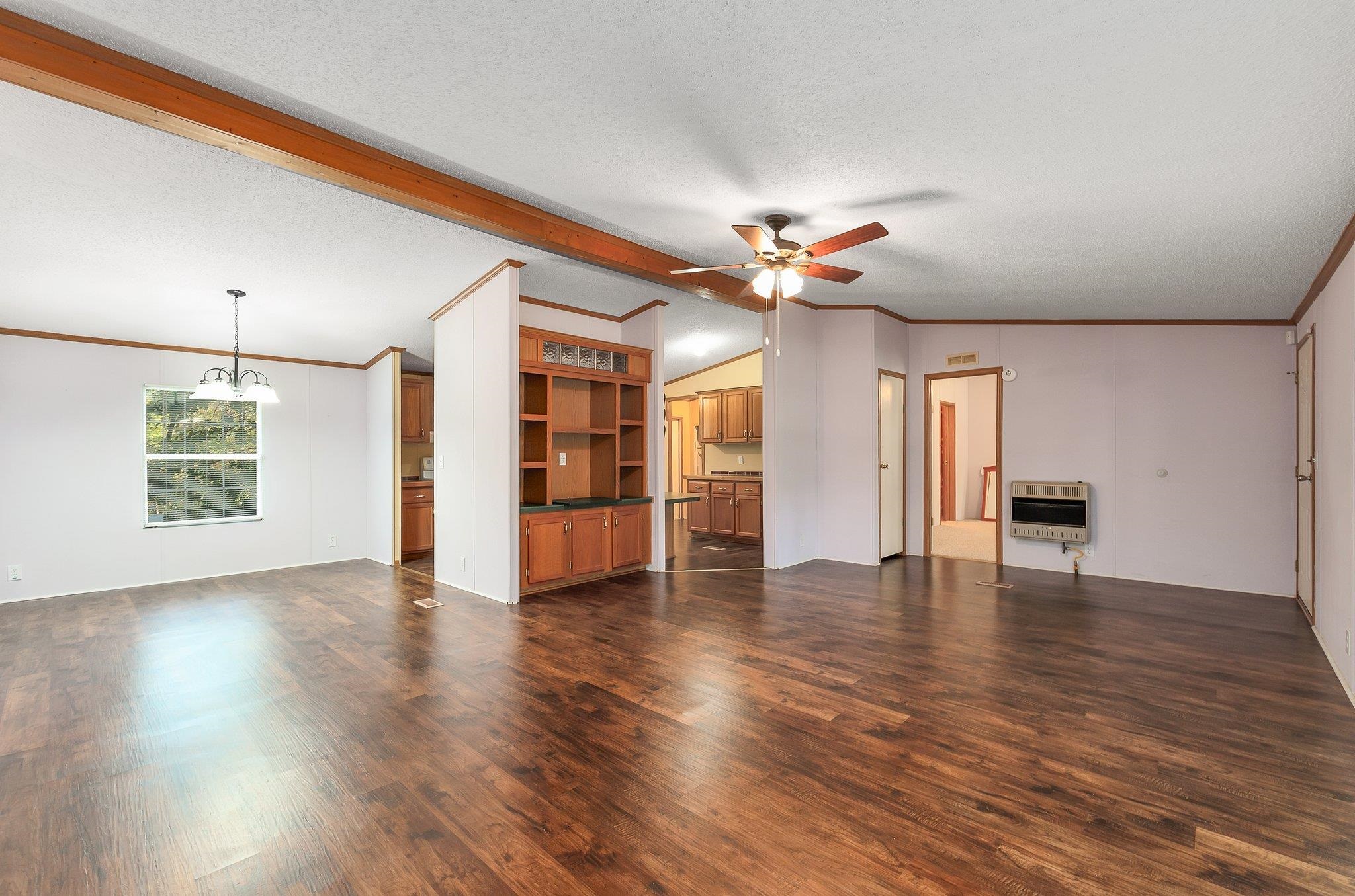 Unfurnished living room featuring ceiling fan with notable chandelier, heating unit, dark hardwood / wood-style floors, ornamental molding, and a textured ceiling