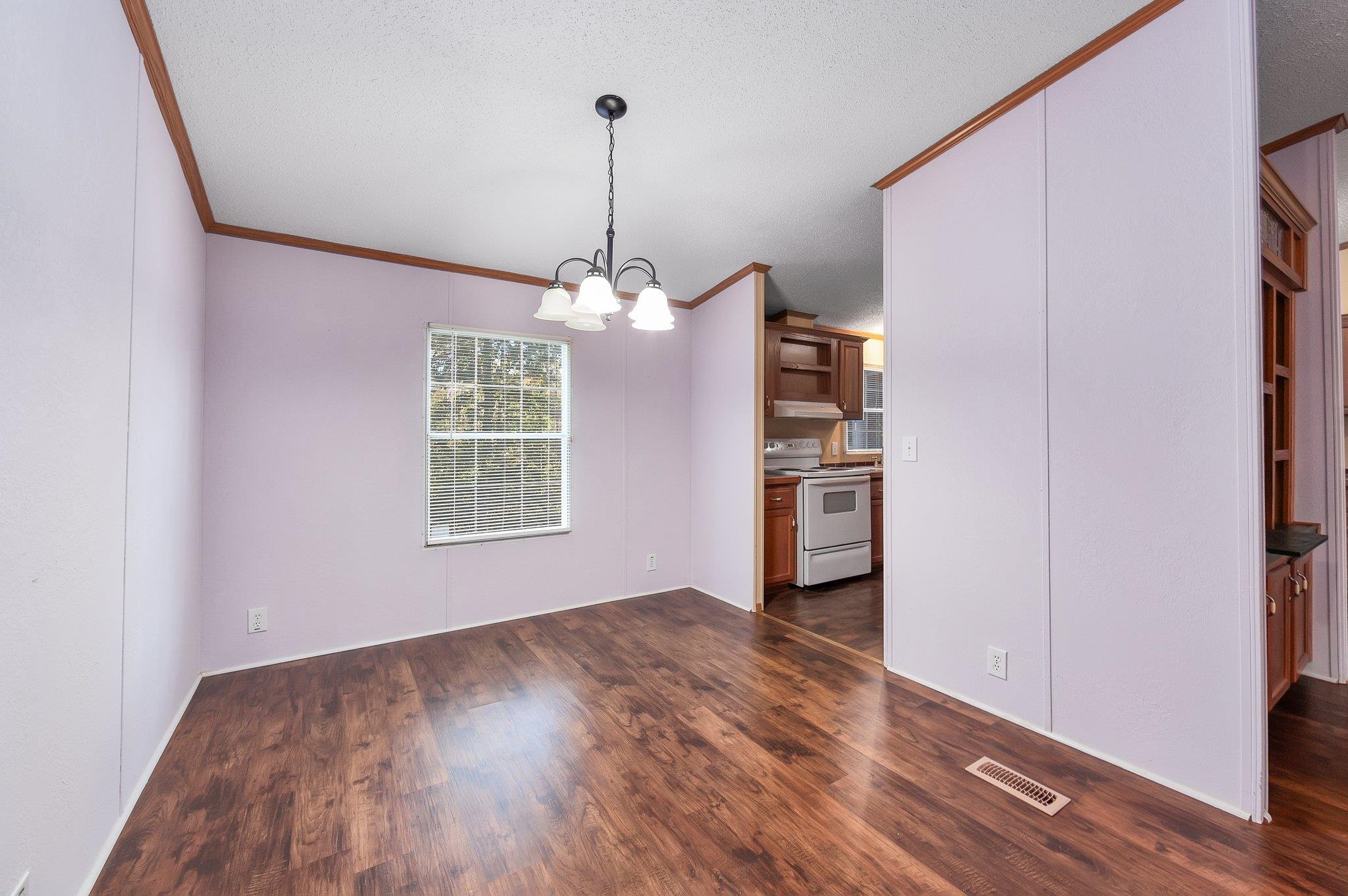 Unfurnished dining area featuring a textured ceiling, a chandelier, dark wood-type flooring, and crown molding