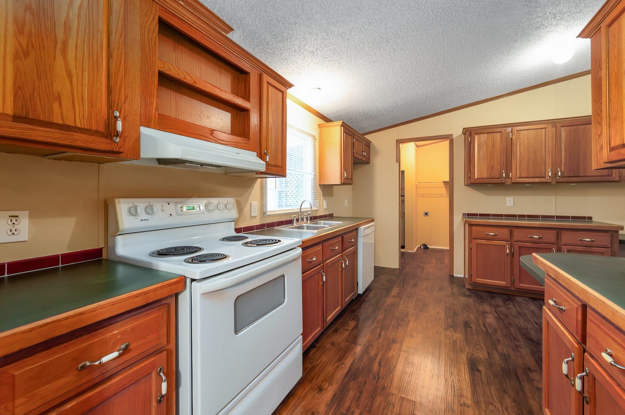 Kitchen featuring lofted ceiling, dark hardwood / wood-style floors, white appliances, ornamental molding, and a textured ceiling