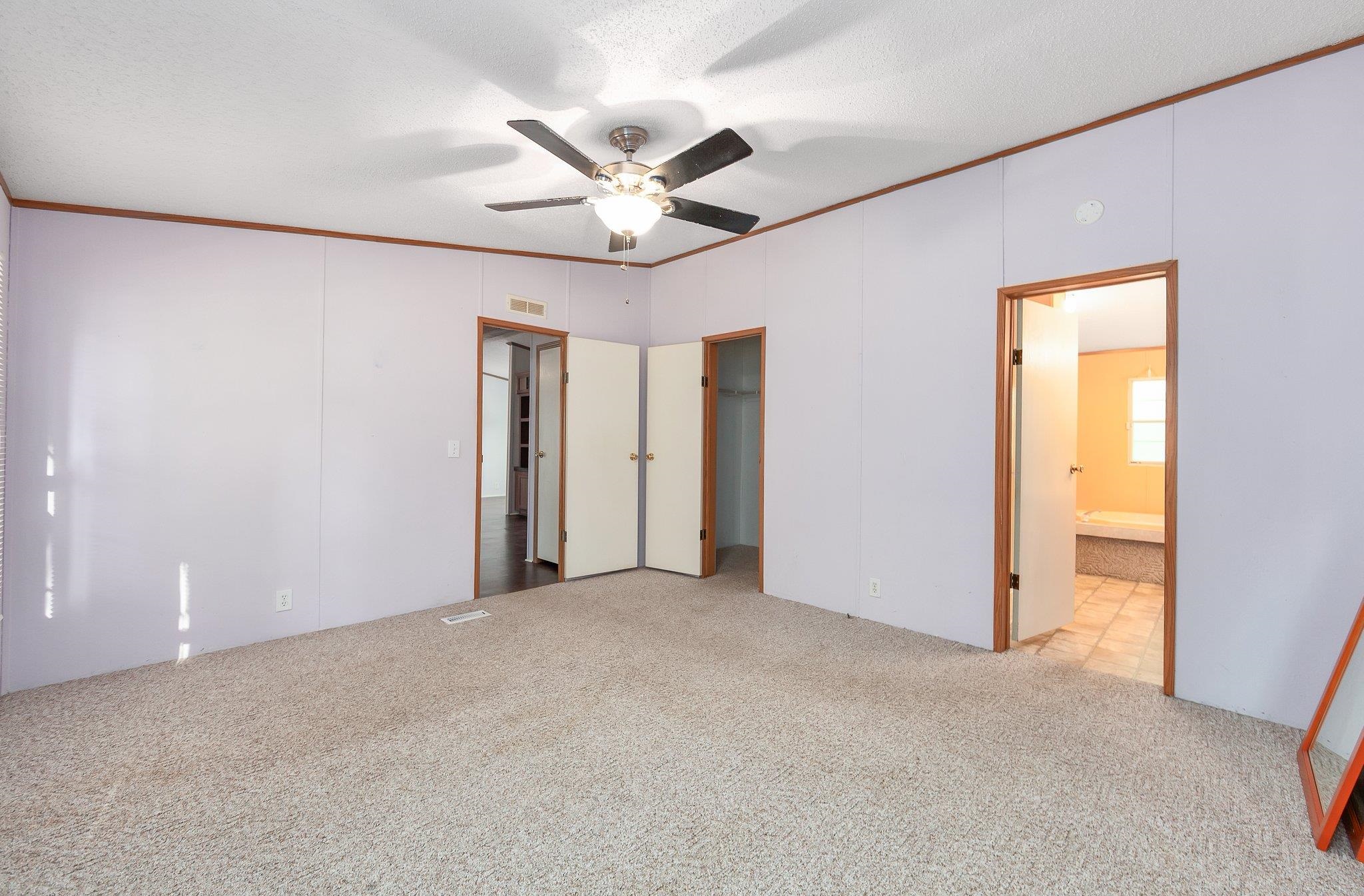 Unfurnished bedroom with ceiling fan, a textured ceiling, light carpet, and ensuite bathroom