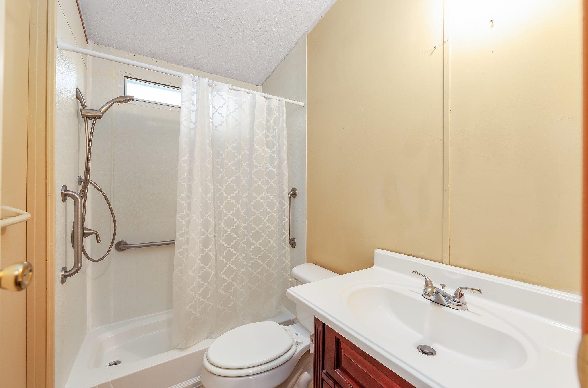 Bathroom with a textured ceiling, walk in shower, vanity, and toilet