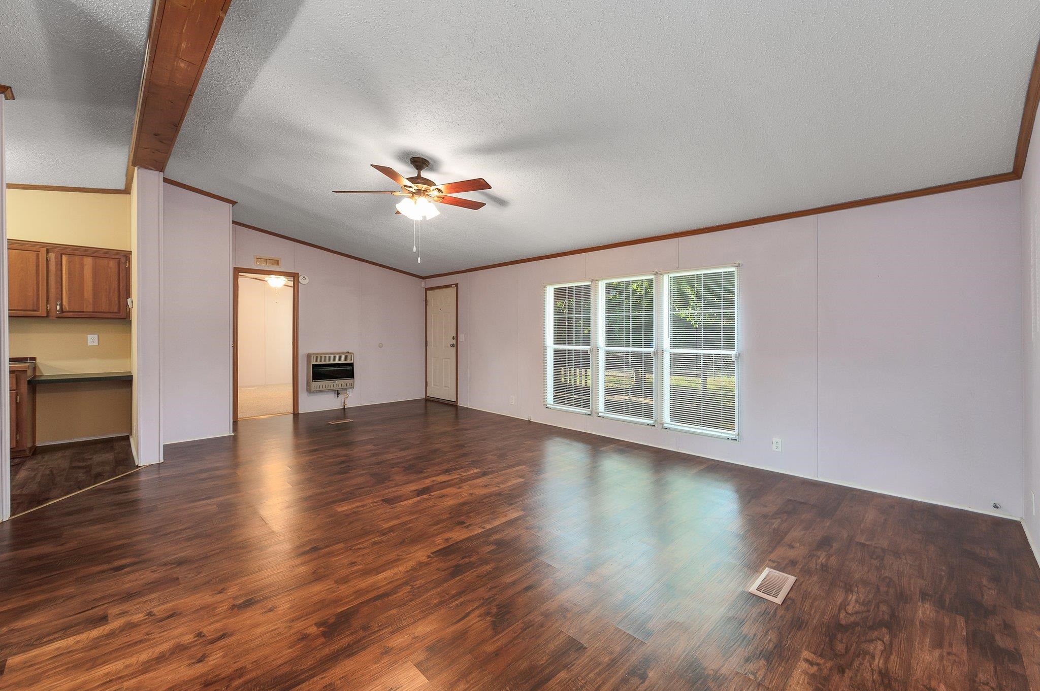 Unfurnished living room with ceiling fan, dark wood-type flooring, heating unit, vaulted ceiling, and a textured ceiling