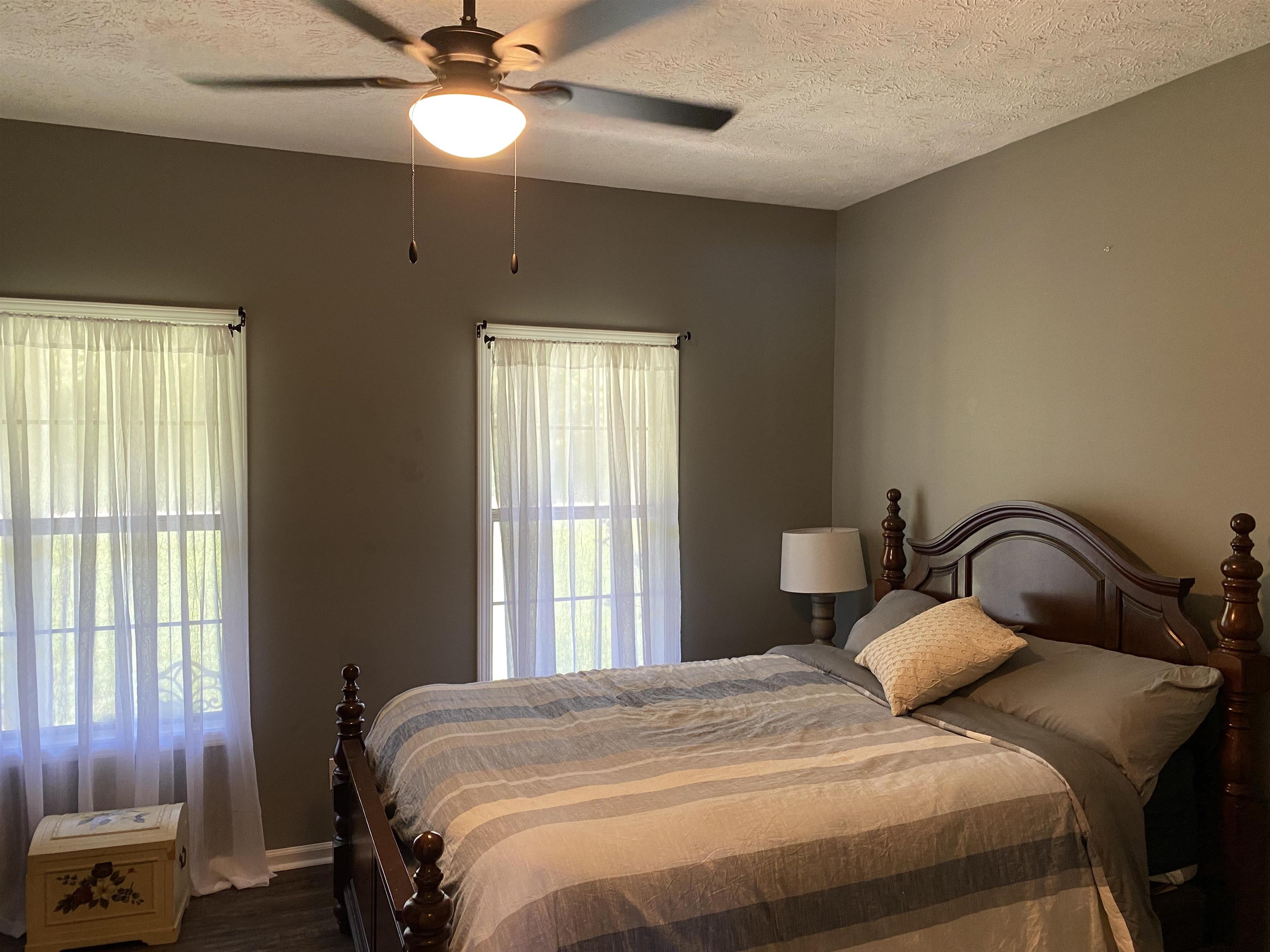 Bedroom with ceiling fan, a textured ceiling, and dark wood-type flooring