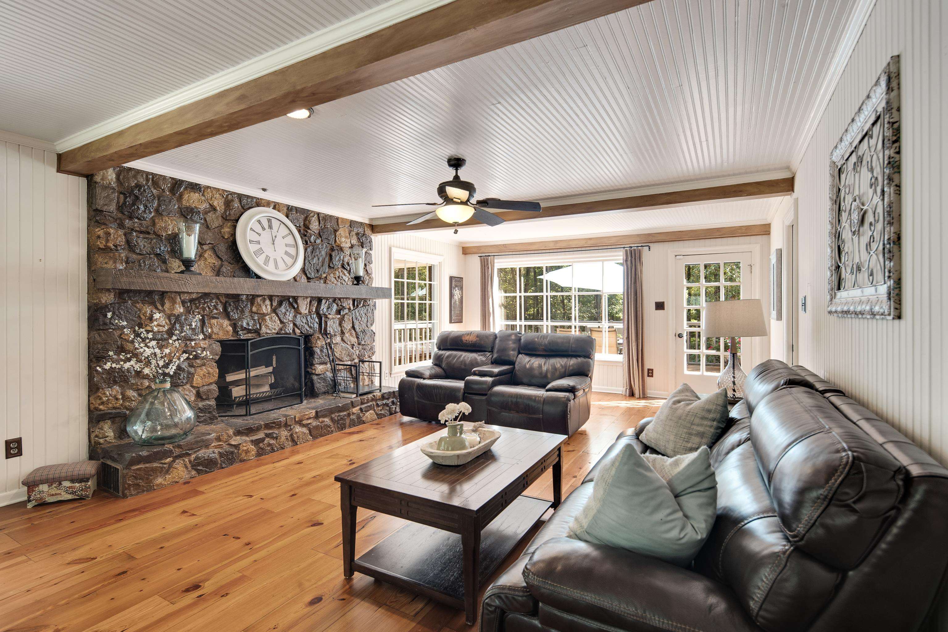 Living room featuring ceiling fan, a stone fireplace, hardwood / wood-style flooring, and wooden walls