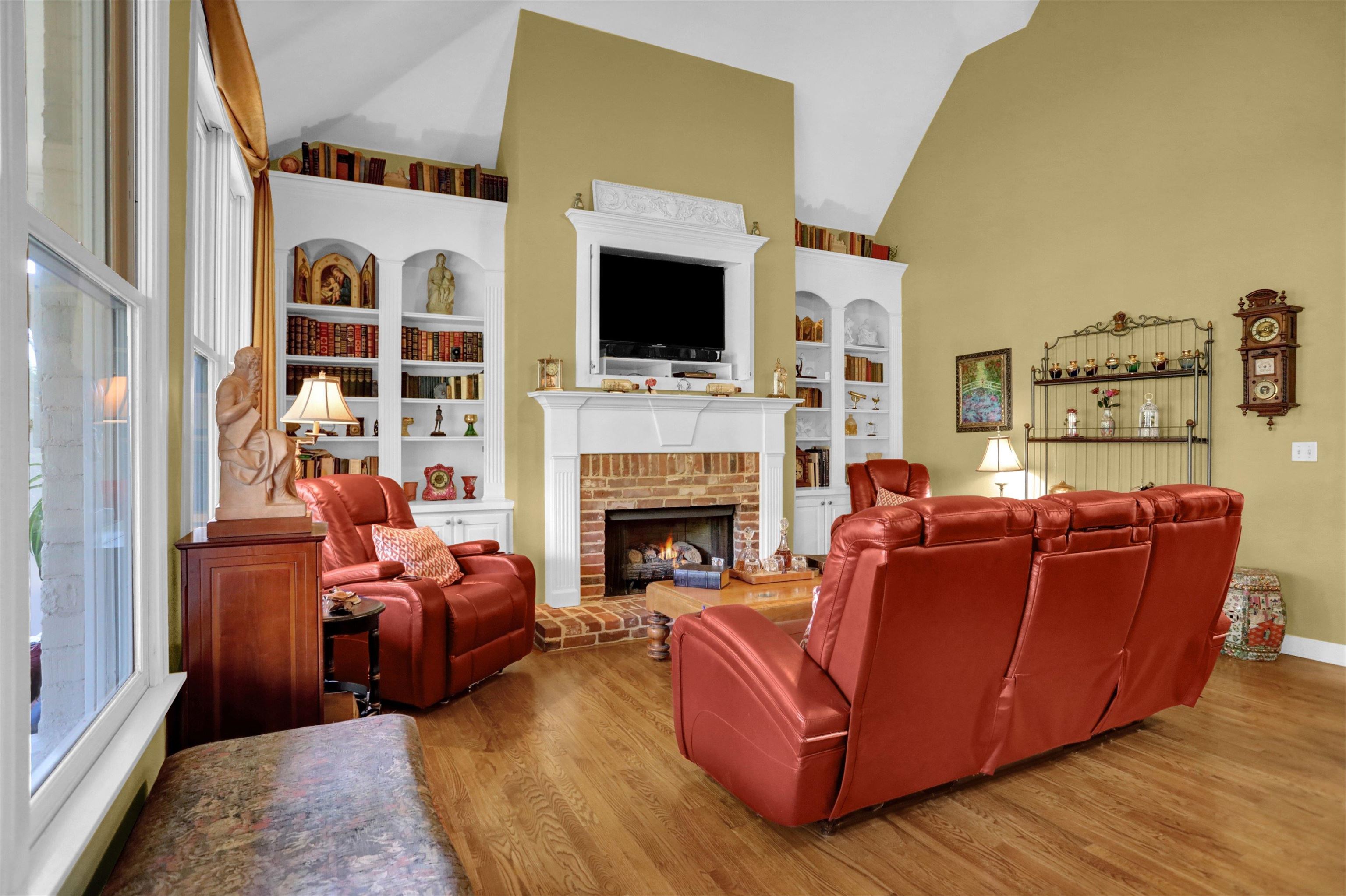 Living room featuring a fireplace, high vaulted ceiling, built in shelves, and light wood-type flooring