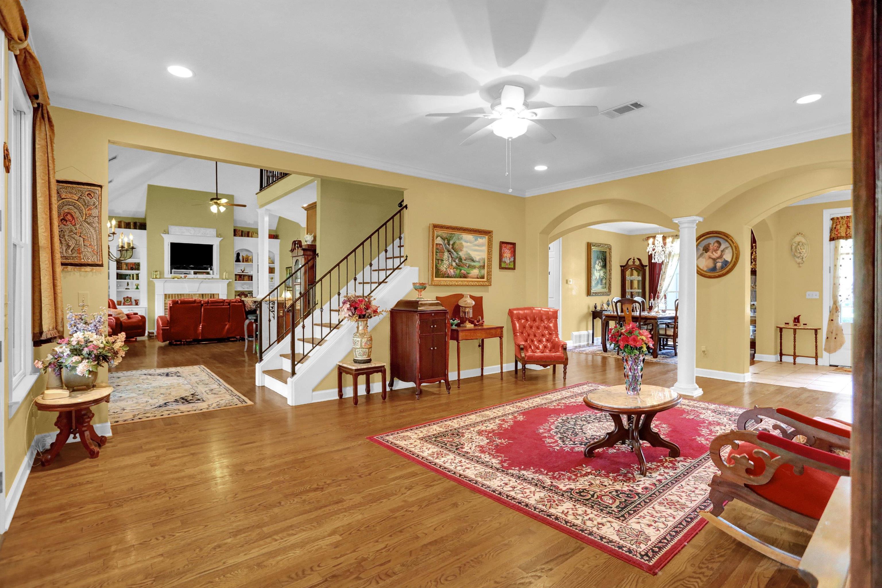 Living room featuring ceiling fan, lofted ceiling, decorative columns, crown molding, and hardwood / wood-style floors