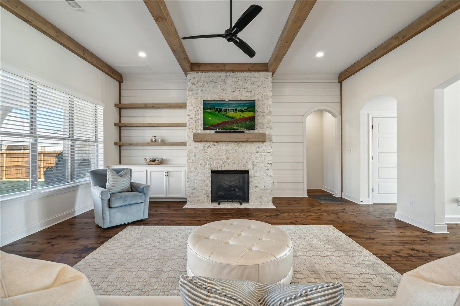 Living room featuring ceiling fan, beamed ceiling, wood walls, a stone fireplace, and dark hardwood / wood-style floors