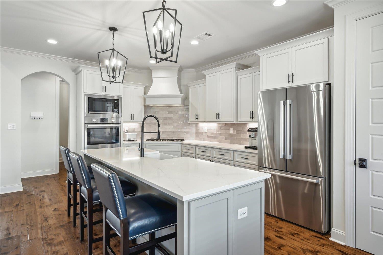 Kitchen featuring white cabinets, stainless steel appliances, decorative light fixtures, a center island with sink, and dark hardwood / wood-style floors