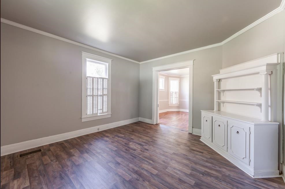 Spare room featuring crown molding and dark wood-type flooring