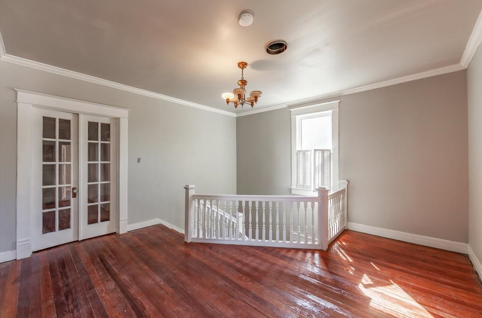 Empty room with french doors, an inviting chandelier, dark hardwood / wood-style floors, and ornamental molding