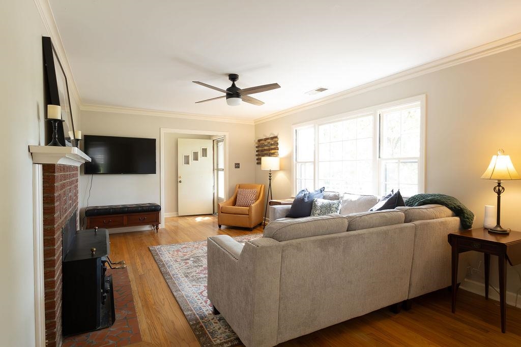 Living room with a brick fireplace, crown molding, hardwood / wood-style flooring, and ceiling fan