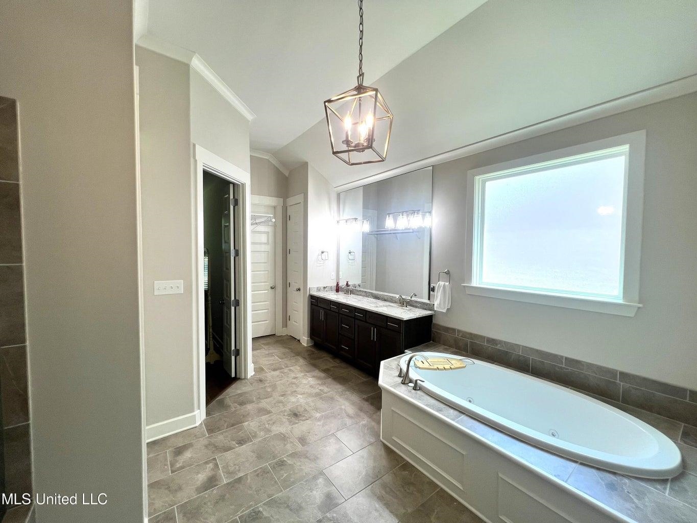 Bathroom featuring lofted ceiling, a bath, an inviting chandelier, and vanity