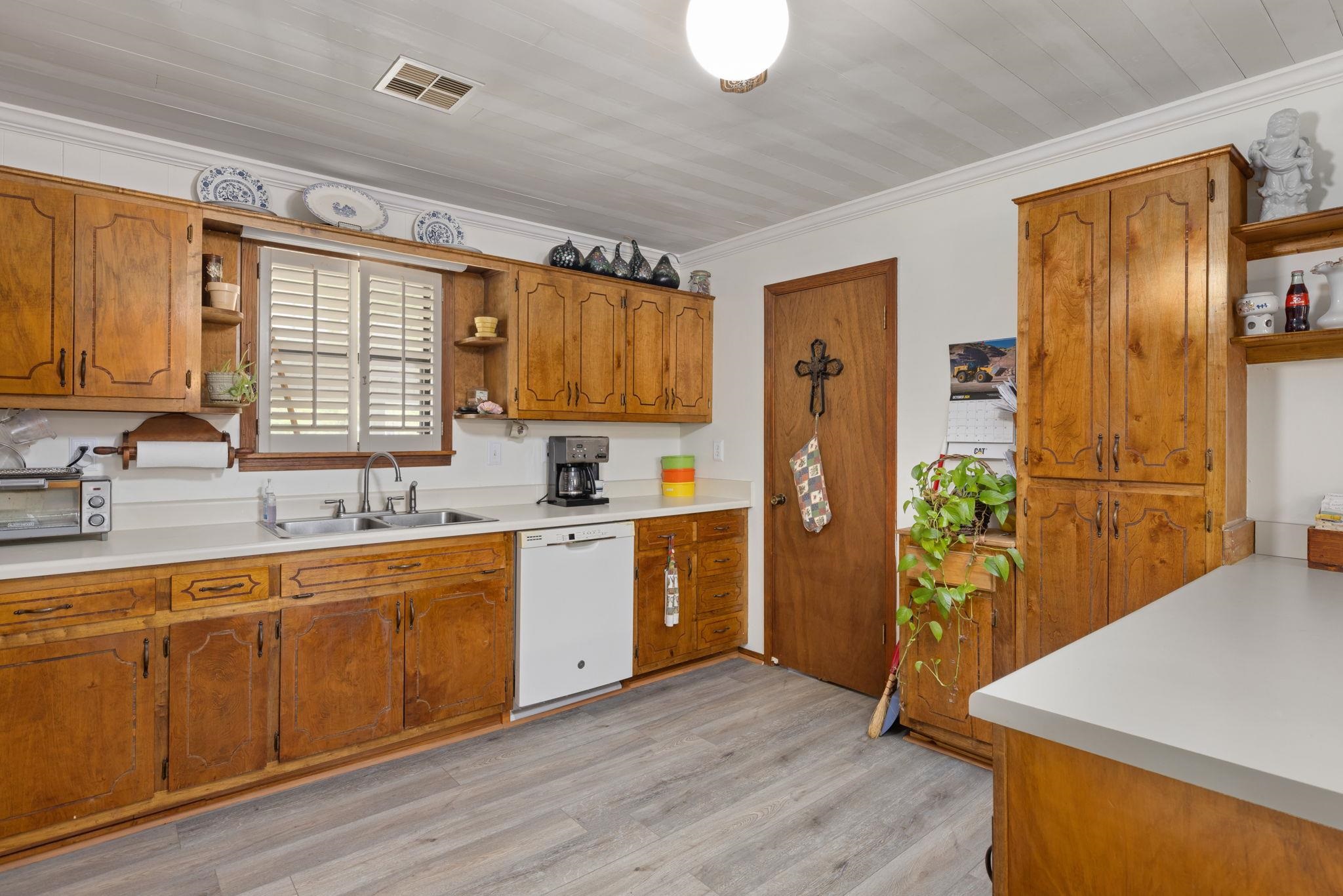 Kitchen with white dishwasher, light hardwood / wood-style floors, crown molding, and sink