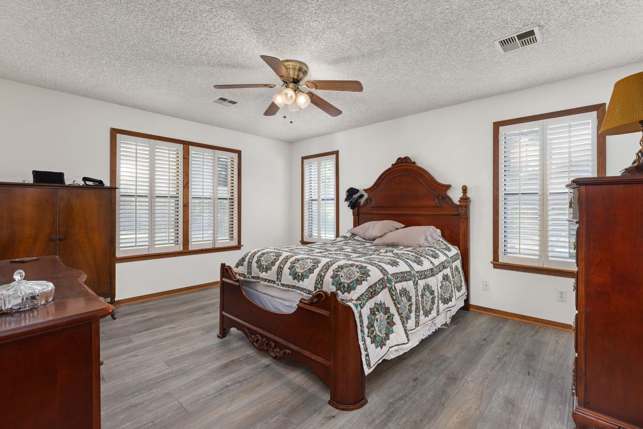 Bedroom featuring a textured ceiling, hardwood / wood-style floors, multiple windows, and ceiling fan