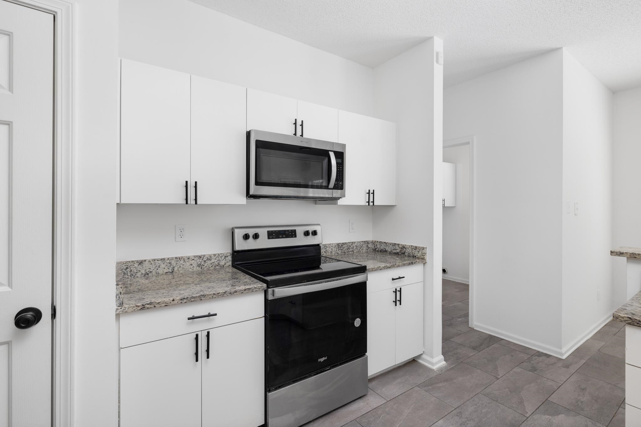 Kitchen with light stone countertops, stainless steel appliances, and white cabinetry