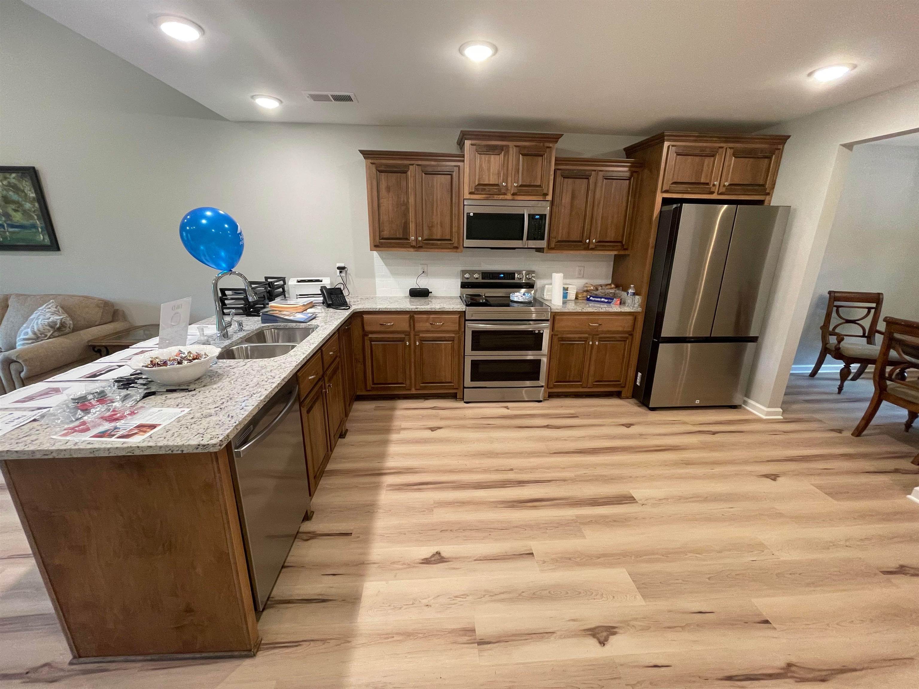 Kitchen with light wood-type flooring, light stone counters, sink, kitchen peninsula, and appliances with stainless steel finishes