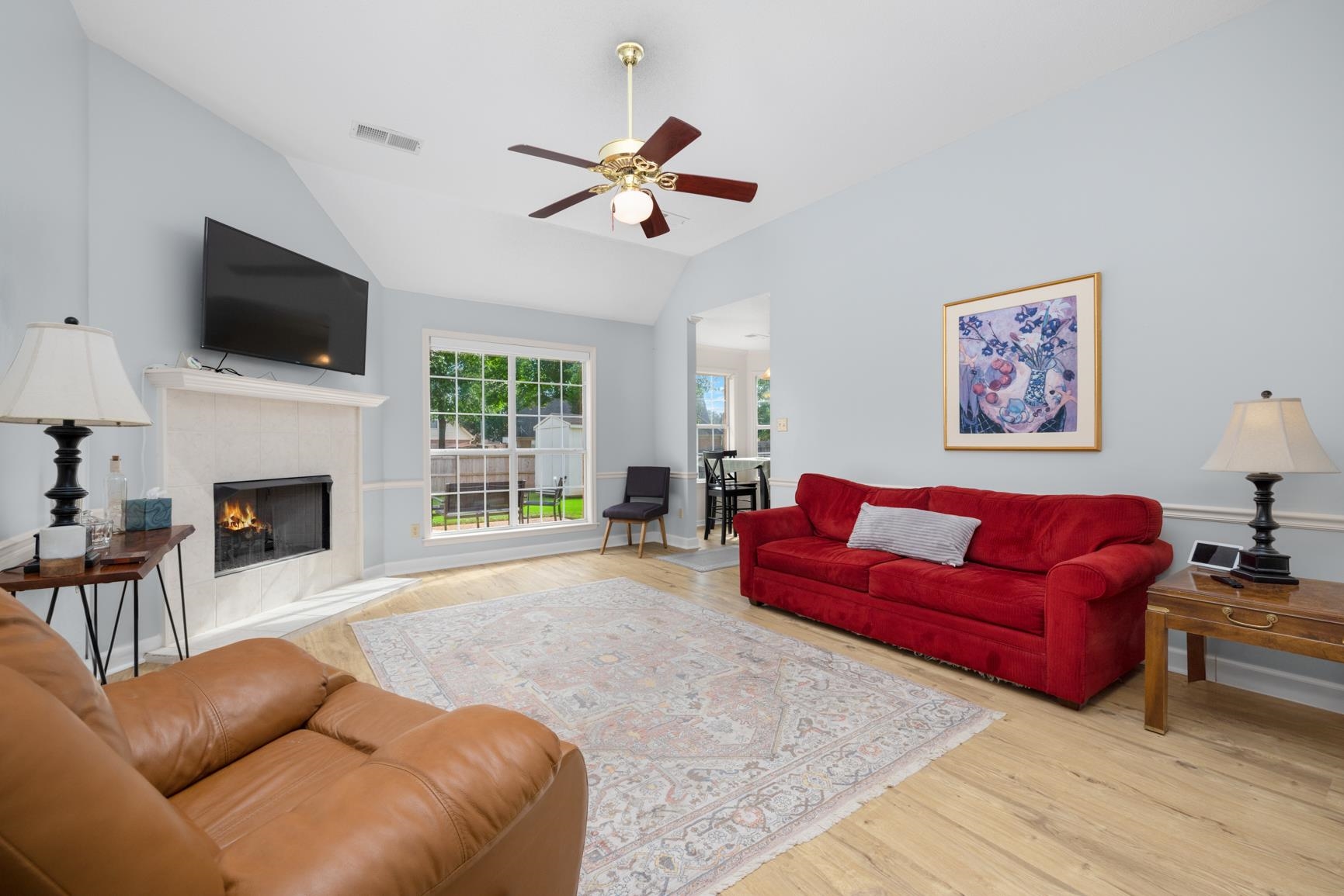 Living room with ceiling fan, lofted ceiling, light wood-type flooring, and a tiled fireplace