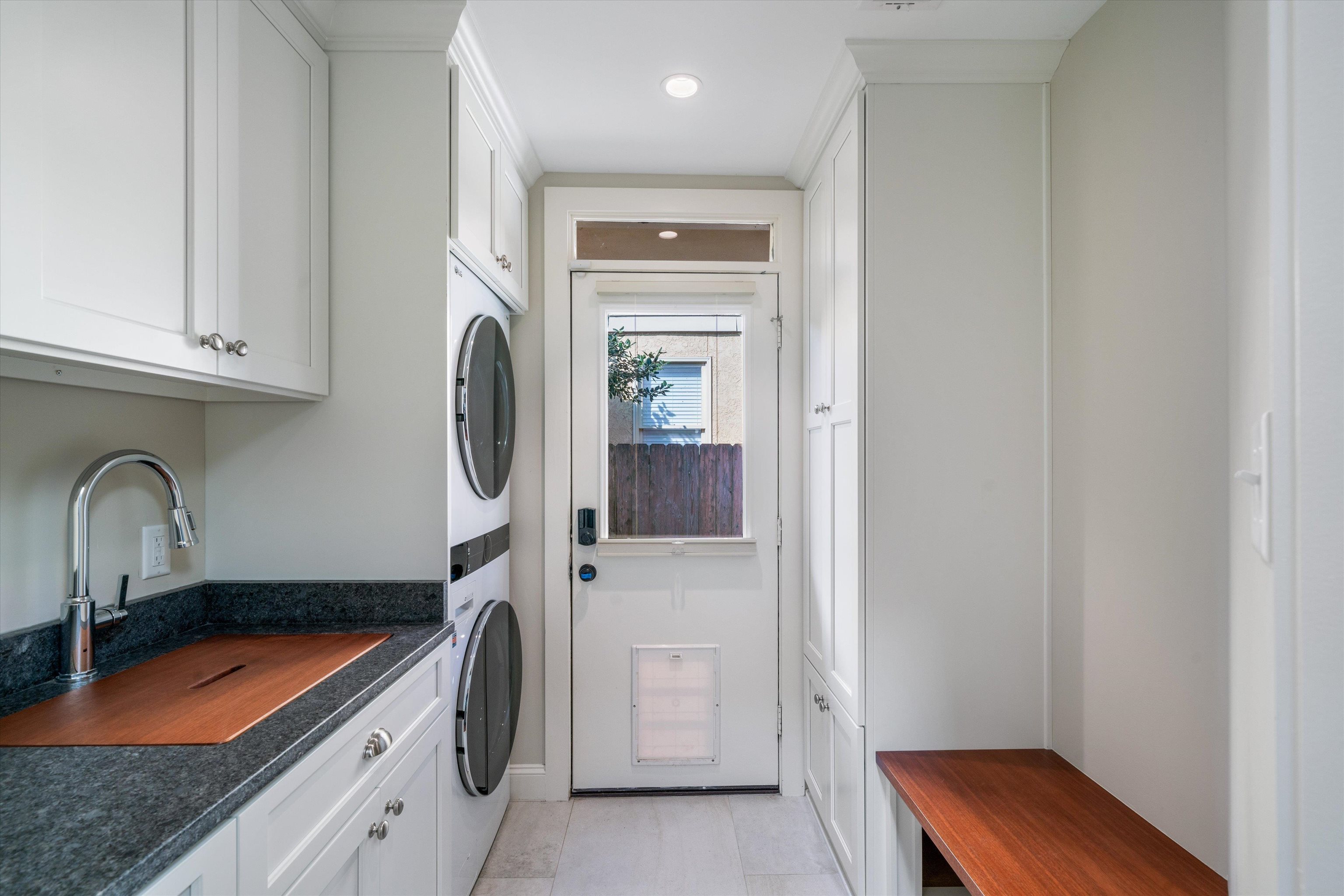 Laundry room with stacked washer and dryer, sink, light tile patterned floors, and cabinets