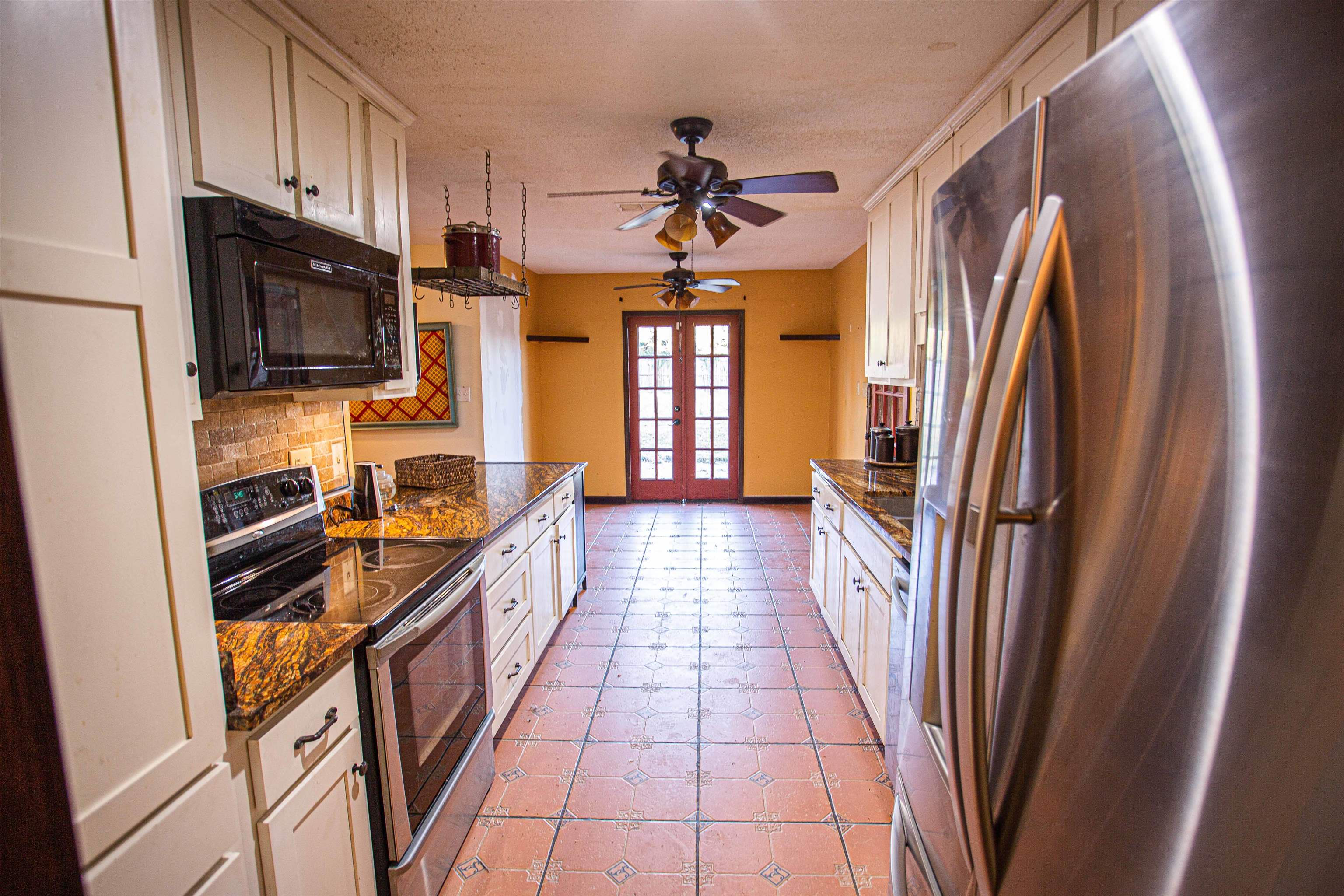 Kitchen featuring ceiling fan, dark stone counters, backsplash, stainless steel appliances, and french doors