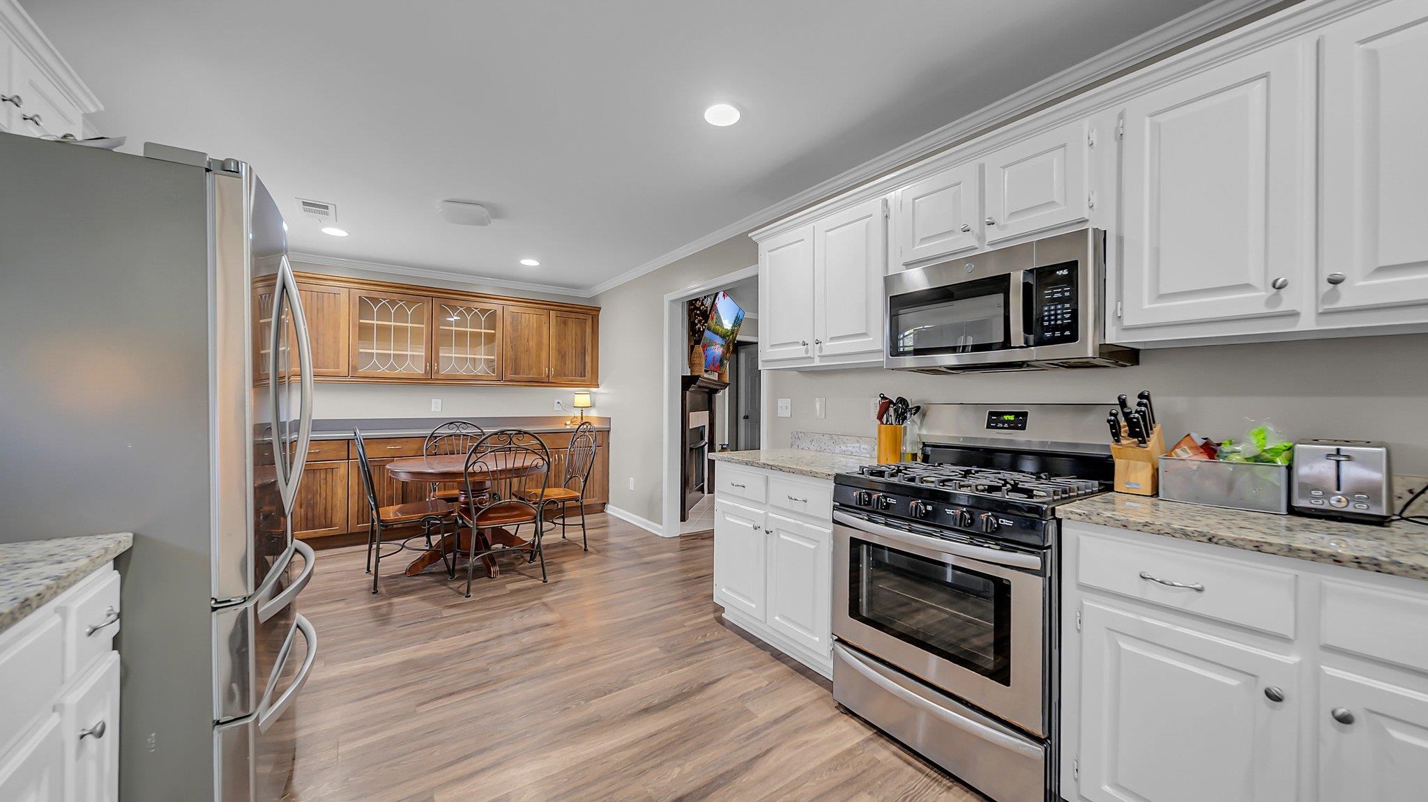 Kitchen with light hardwood / wood-style floors, crown molding, light stone countertops, appliances with stainless steel finishes, and white cabinetry