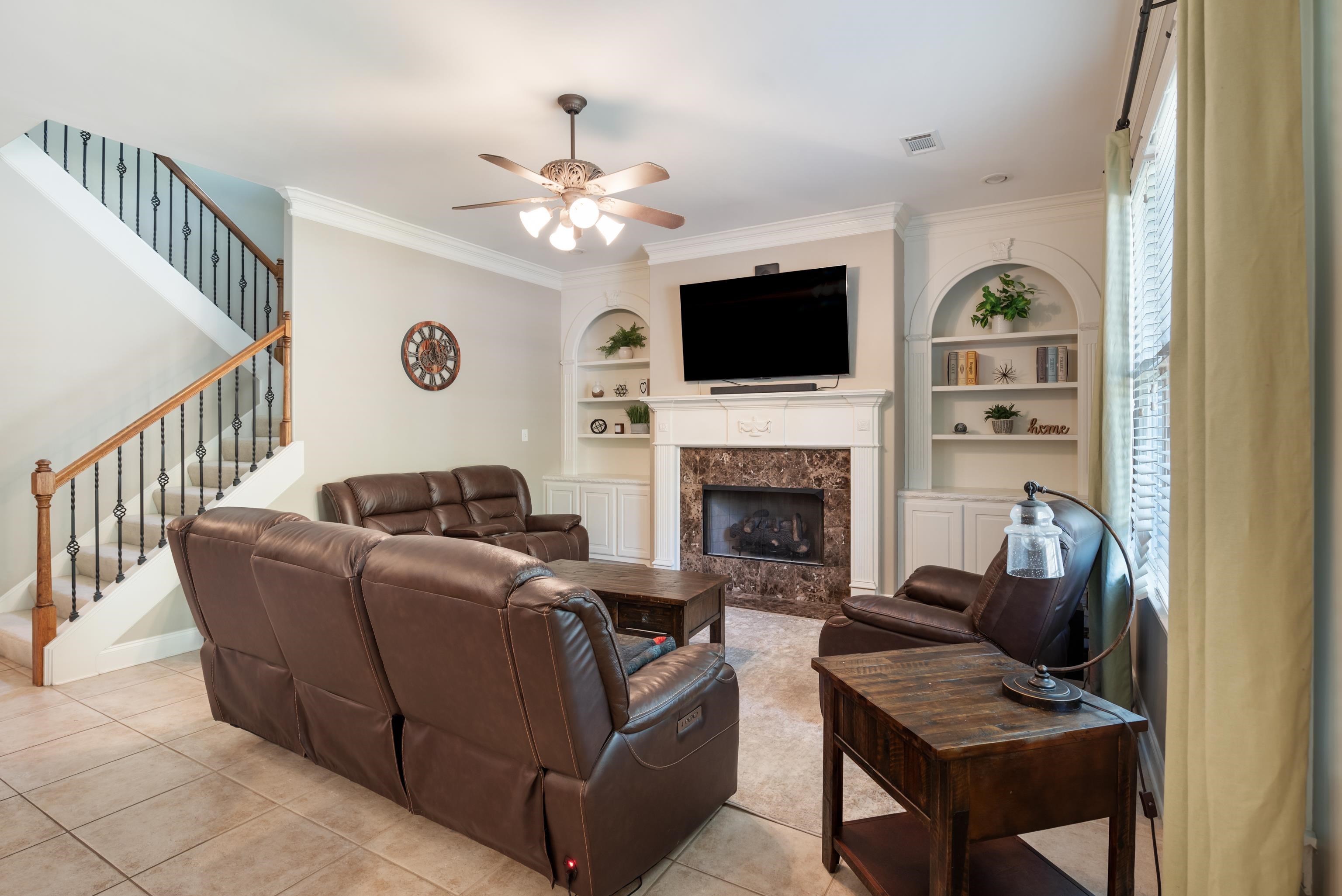 Tiled living room featuring built in shelves, a fireplace, ornamental molding, and ceiling fan