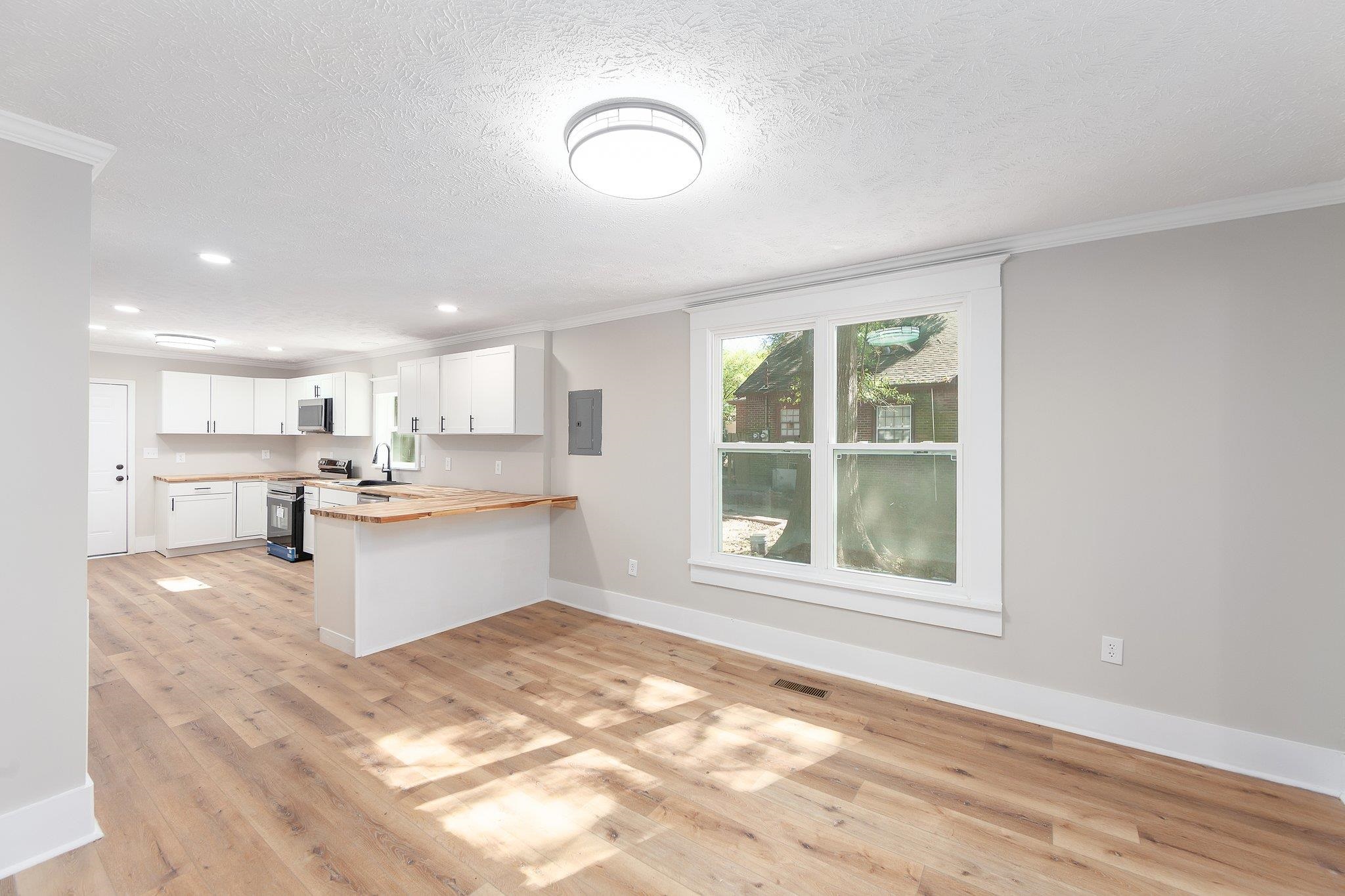 Kitchen with kitchen peninsula, electric range, white cabinetry, light hardwood / wood-style floors, and butcher block countertops