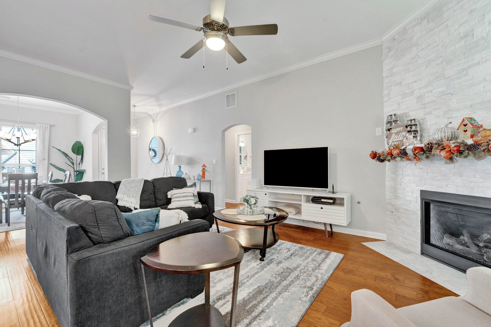 Living room featuring ornamental molding, a fireplace, hardwood / wood-style flooring, and ceiling fan with notable chandelier