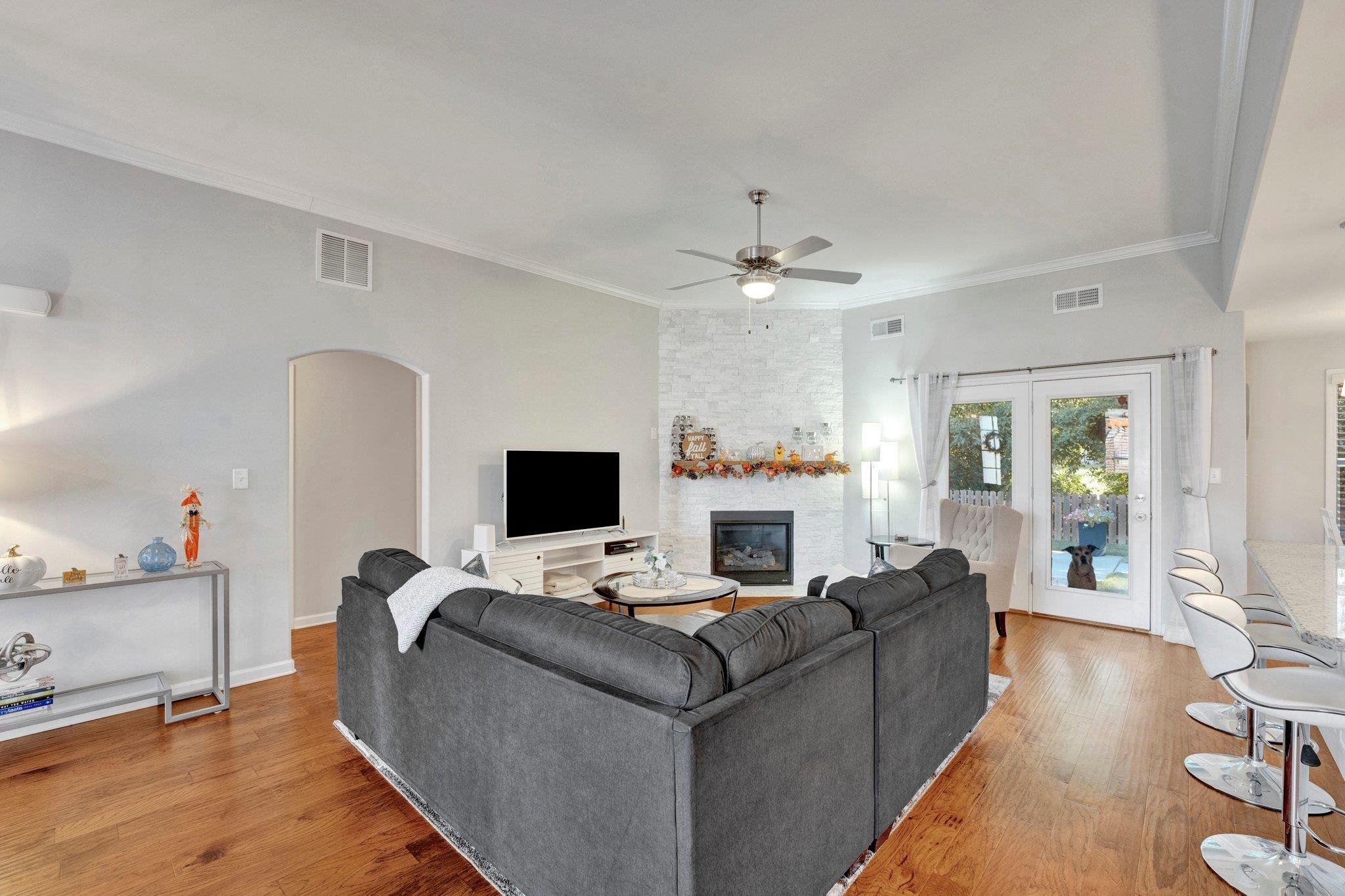 Living room with a stone fireplace, crown molding, hardwood / wood-style floors, and ceiling fan