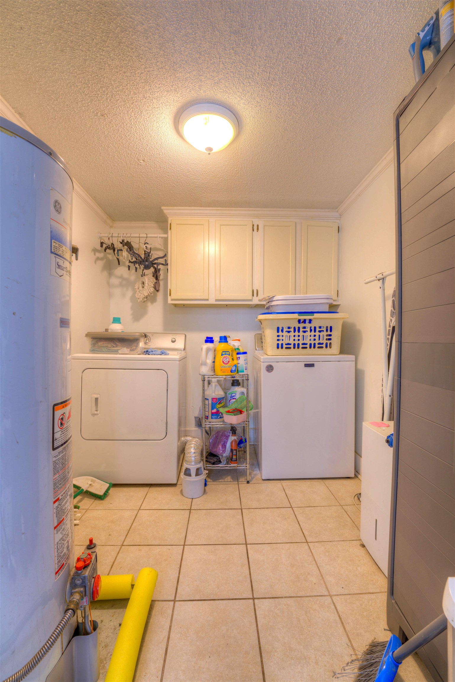 Washroom with washer and clothes dryer, cabinets, gas water heater, and a textured ceiling