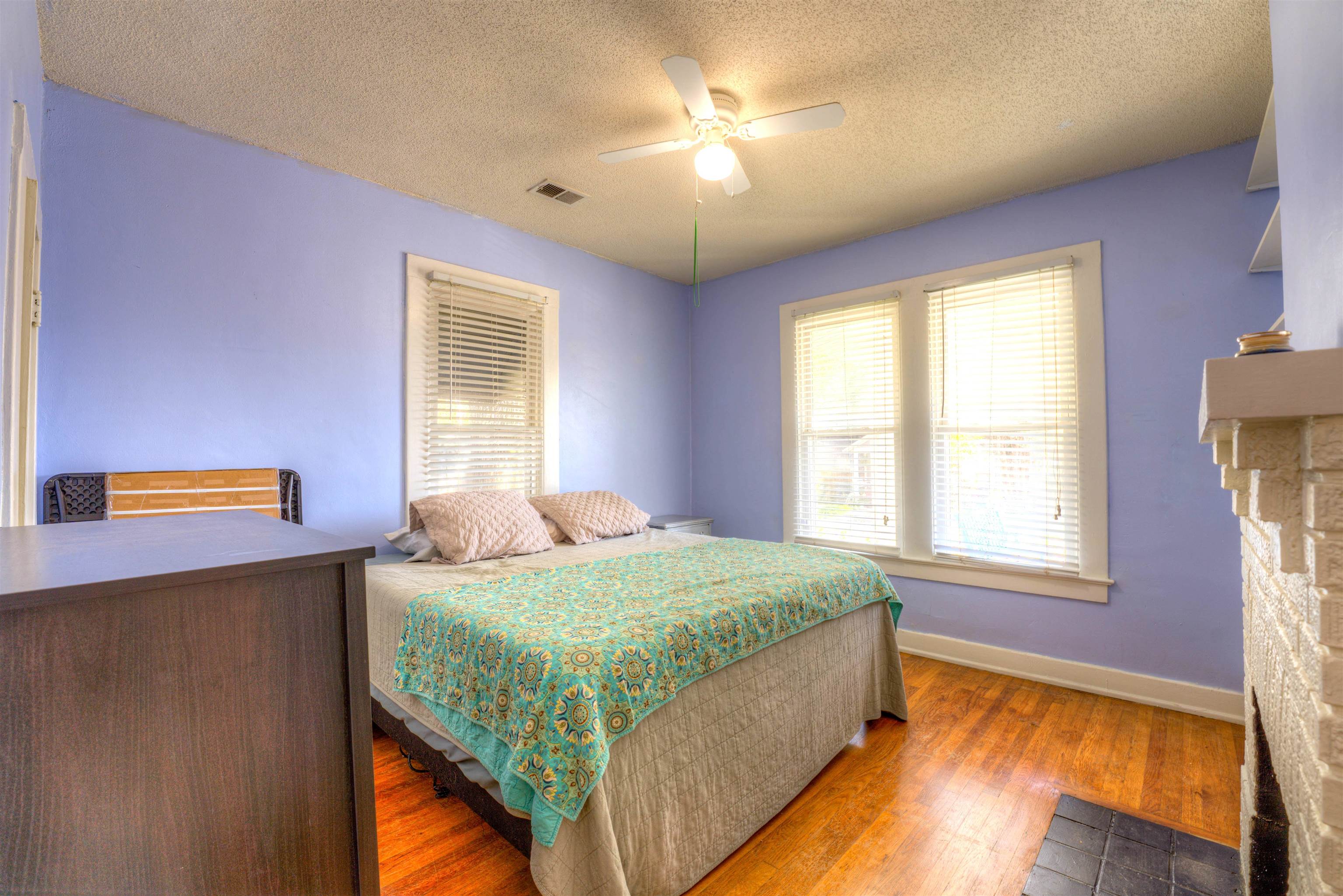 Bedroom featuring a stone fireplace, hardwood / wood-style floors, a textured ceiling, and ceiling fan