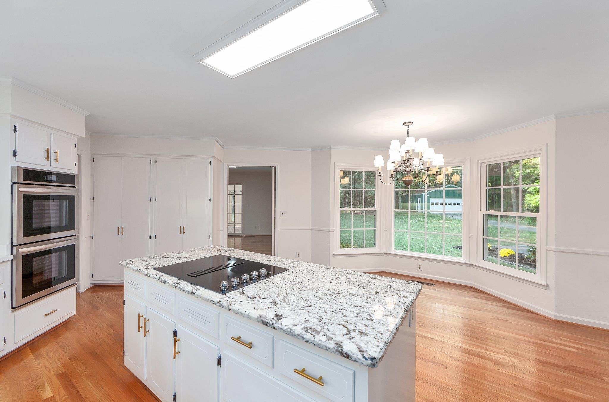 Kitchen with light wood-type flooring, a kitchen island, stainless steel double oven, black electric cooktop, and white cabinetry