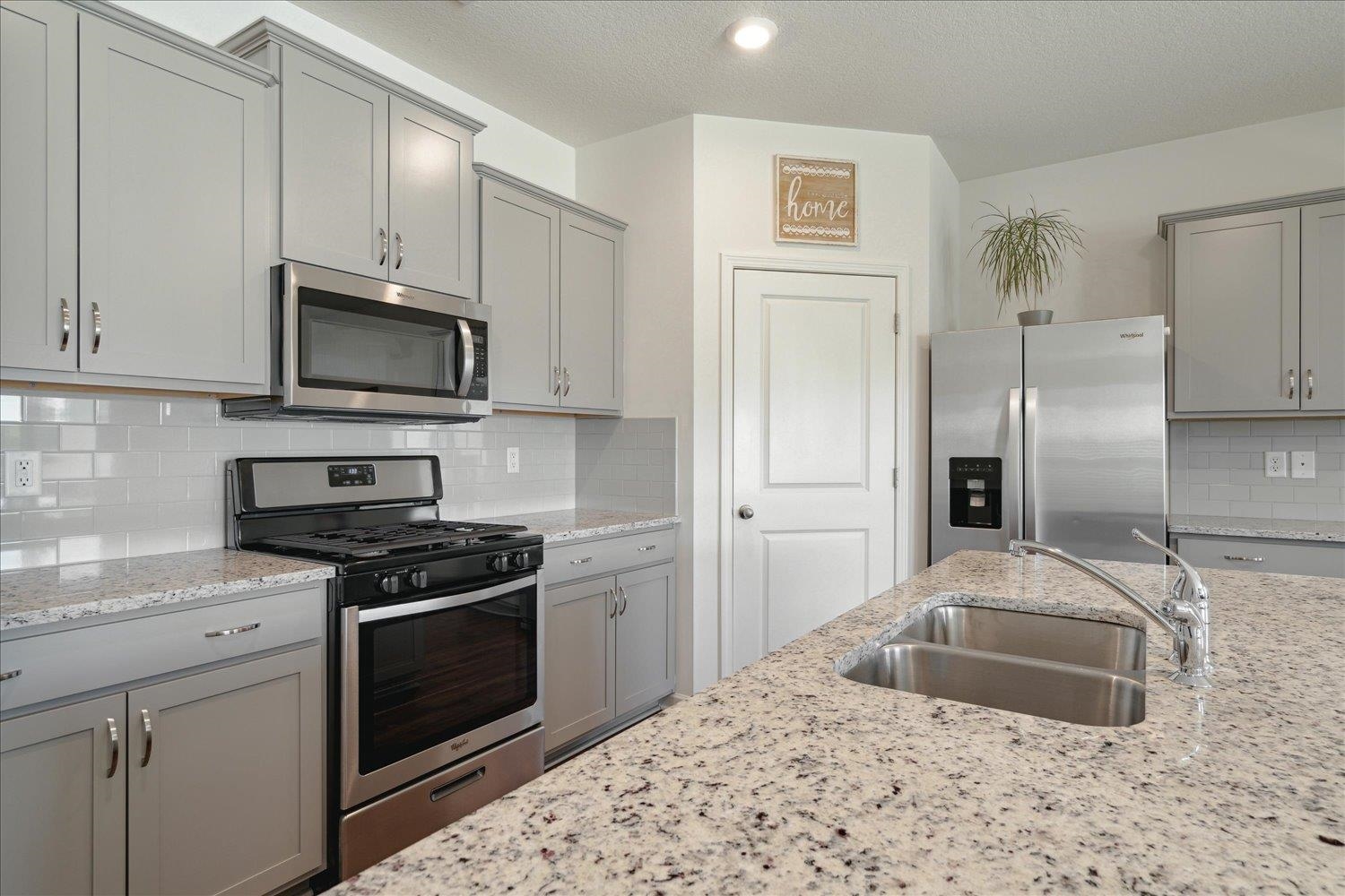 Kitchen featuring light stone countertops, sink, appliances with stainless steel finishes, and backsplash