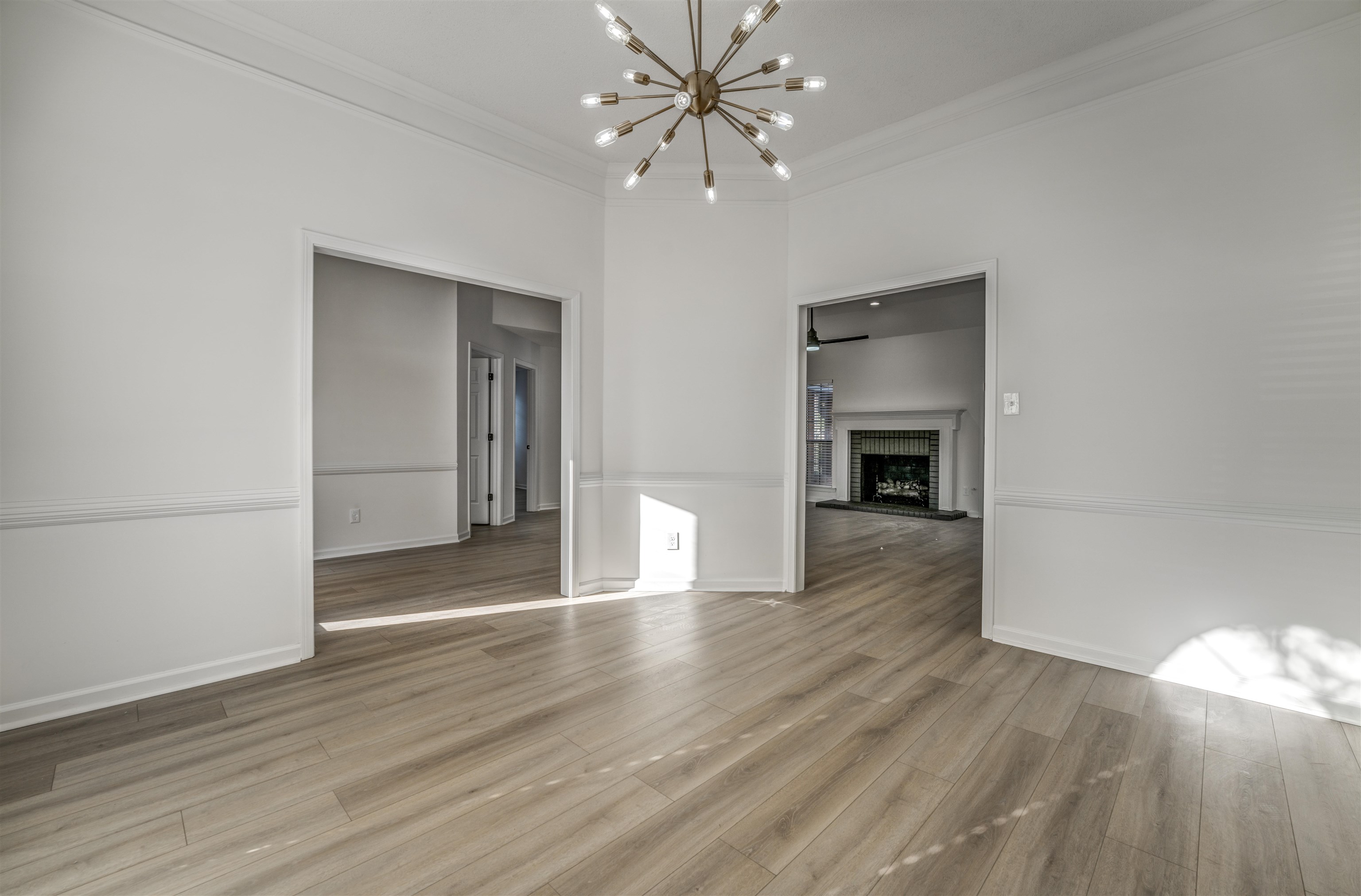 Unfurnished living room with light hardwood / wood-style flooring, ornamental molding, a notable chandelier, and a brick fireplace