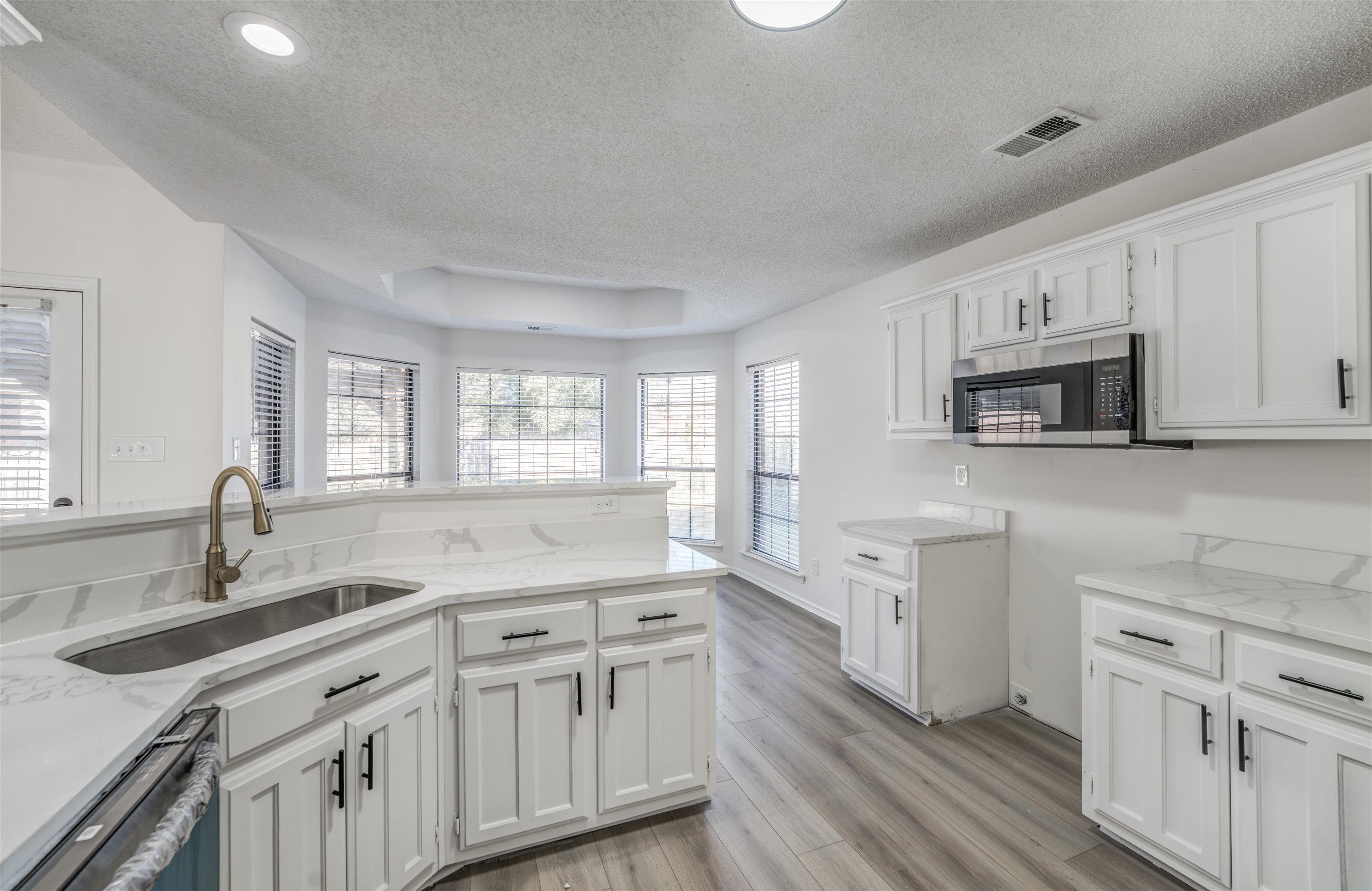 Kitchen with white cabinets, a textured ceiling, light hardwood / wood-style flooring, dishwasher, and sink