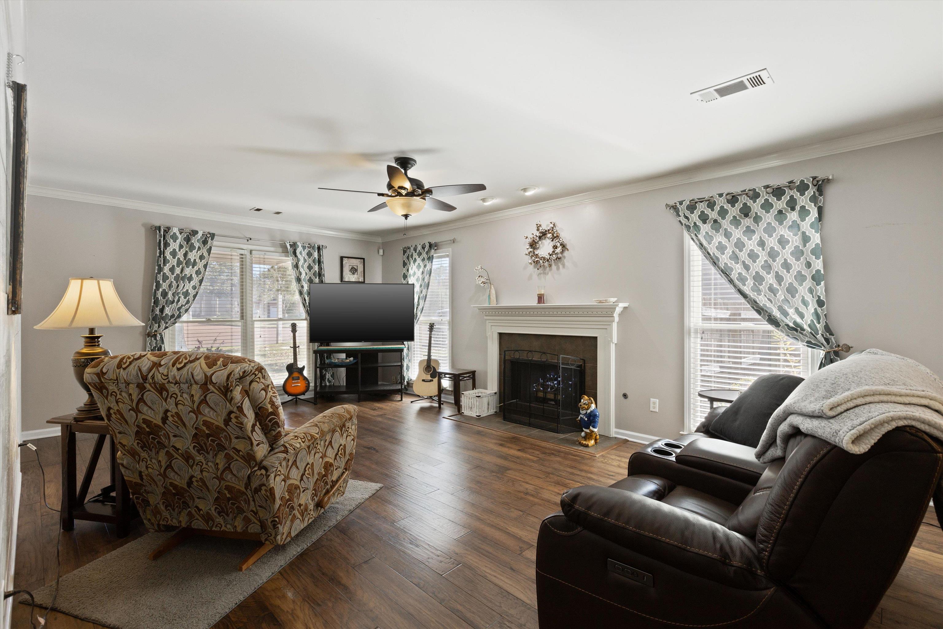 Living room with ornamental molding, dark hardwood / wood-style floors, a tiled fireplace, and ceiling fan