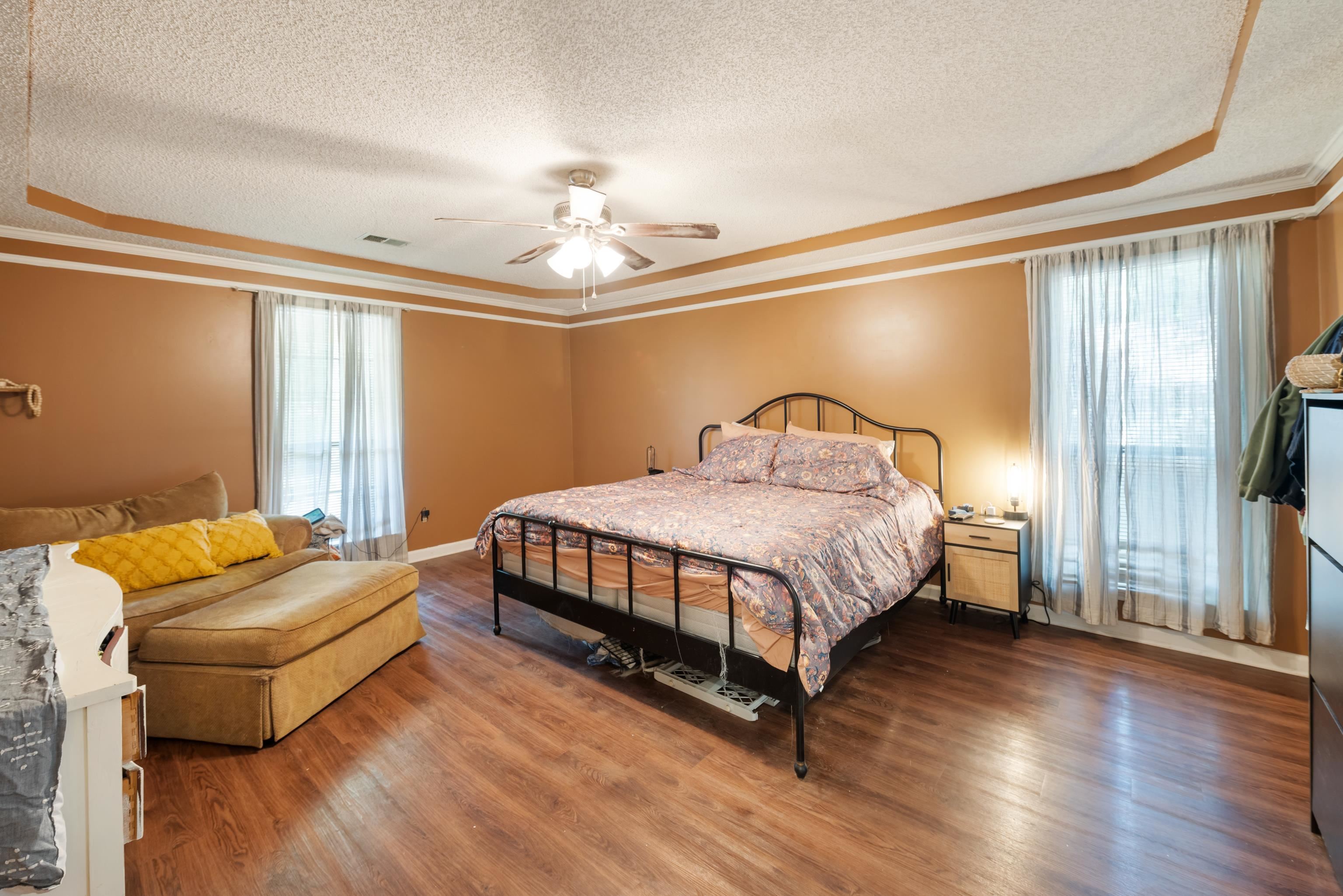 Bedroom featuring ceiling fan, a tray ceiling, multiple windows, and hardwood / wood-style floors