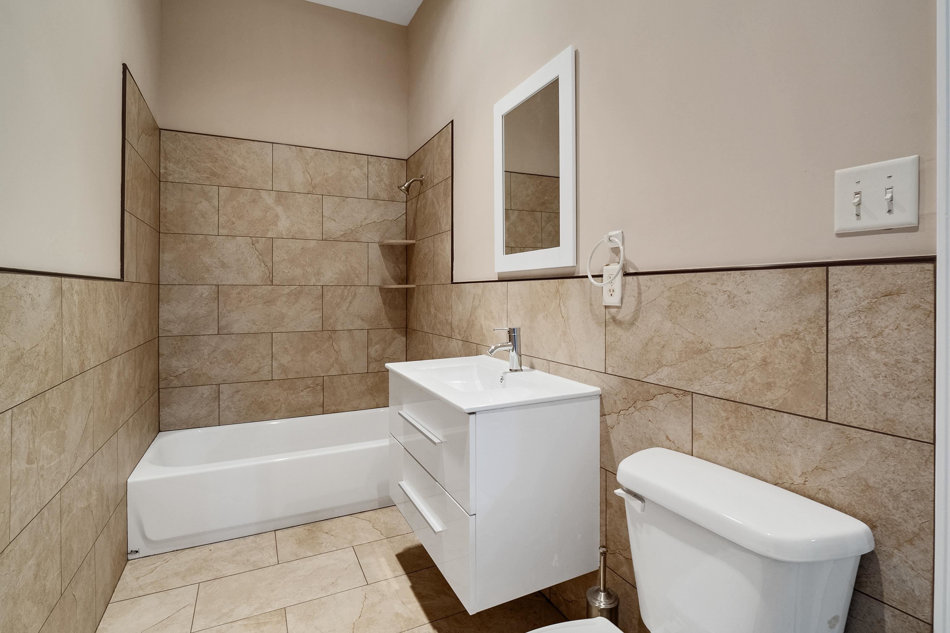 Full bathroom featuring tile walls, toilet, vanity, tiled shower / bath combo, and tile patterned flooring