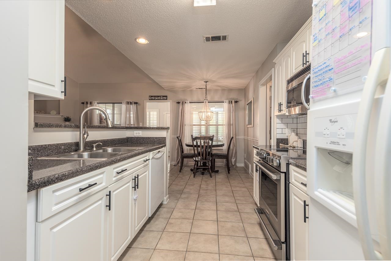 Kitchen featuring stainless steel appliances, sink, light tile patterned flooring, decorative light fixtures, and white cabinets